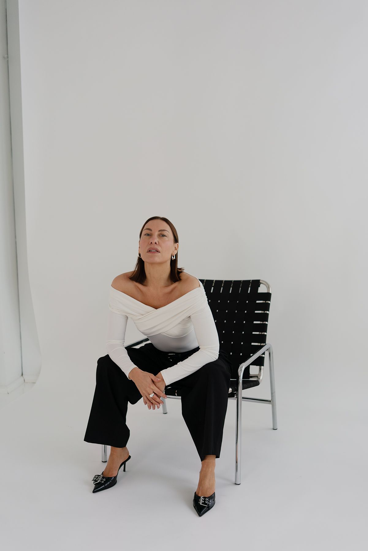 Stylish outfit featuring white top, black pants and pointed heels in a minimalist studio setting.