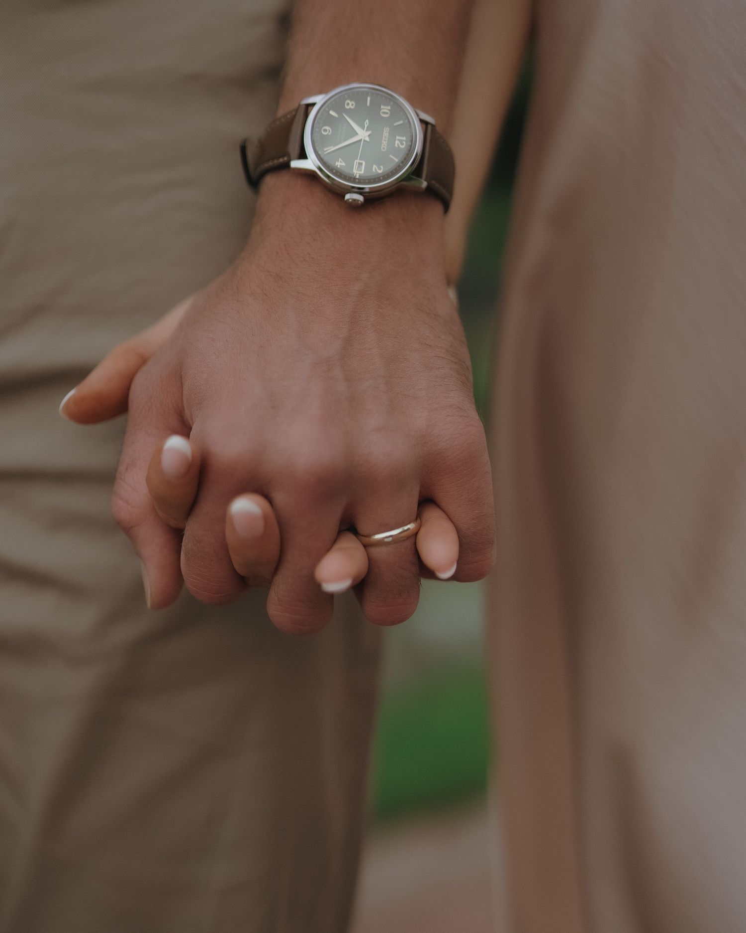 Two hands tenderly clasped together, one wearing a classic watch with a leather band displaying midsummer time.