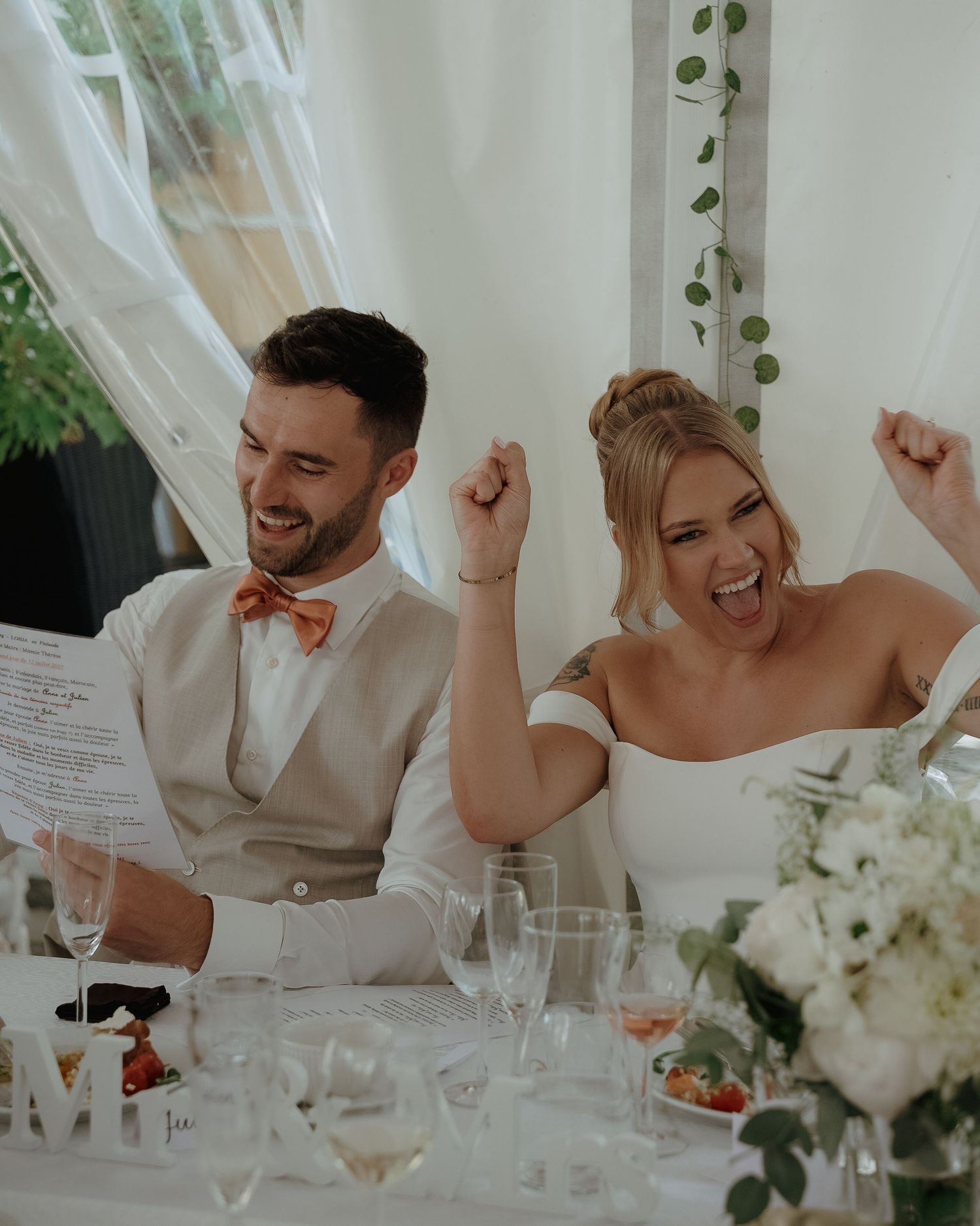 A joyful couple celebrates during their wedding reception, surrounded by white florals and elegant table settings.