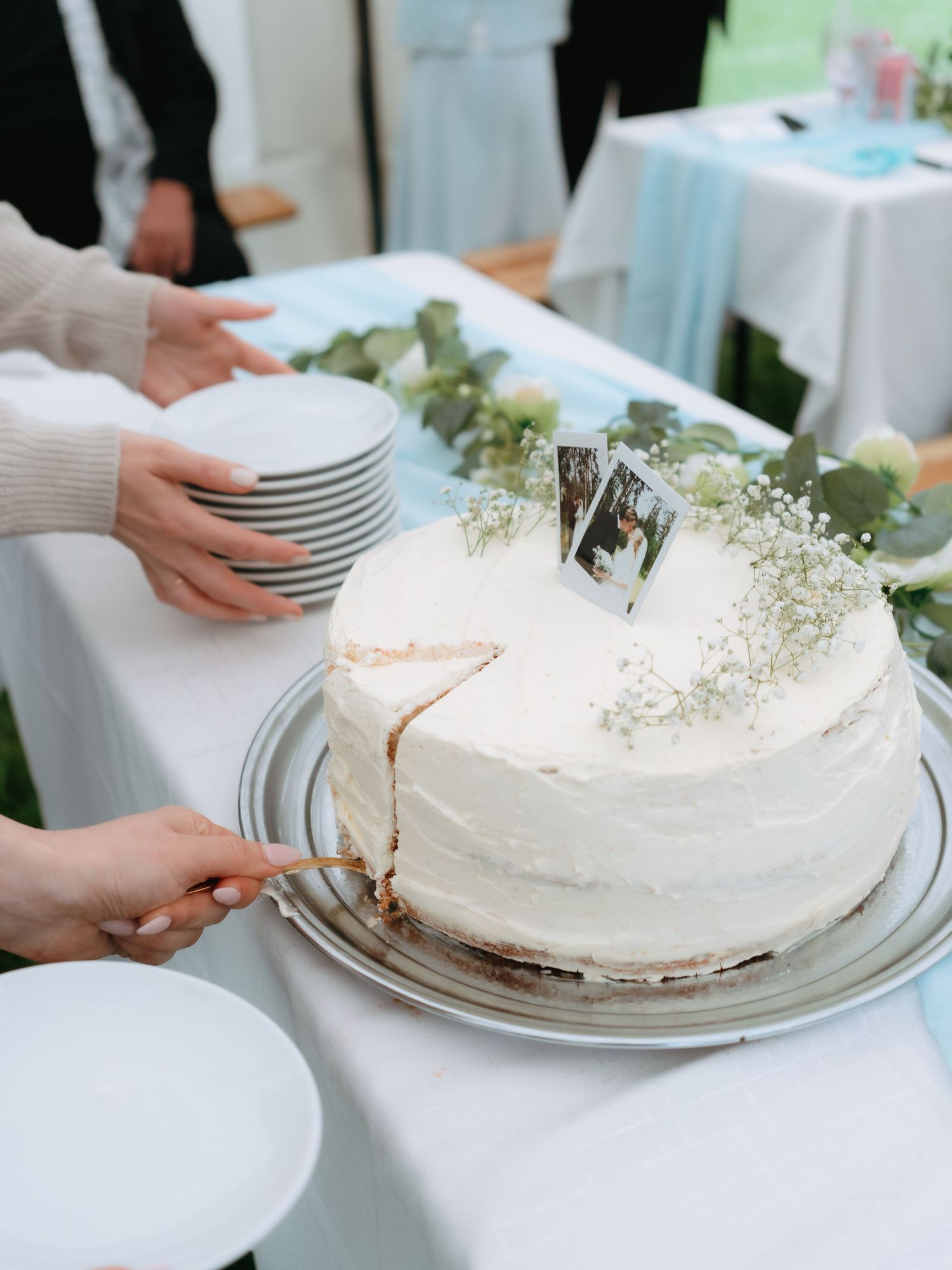 Close-up of white wedding cake being sliced with photo topper and baby's breath floral decoration.