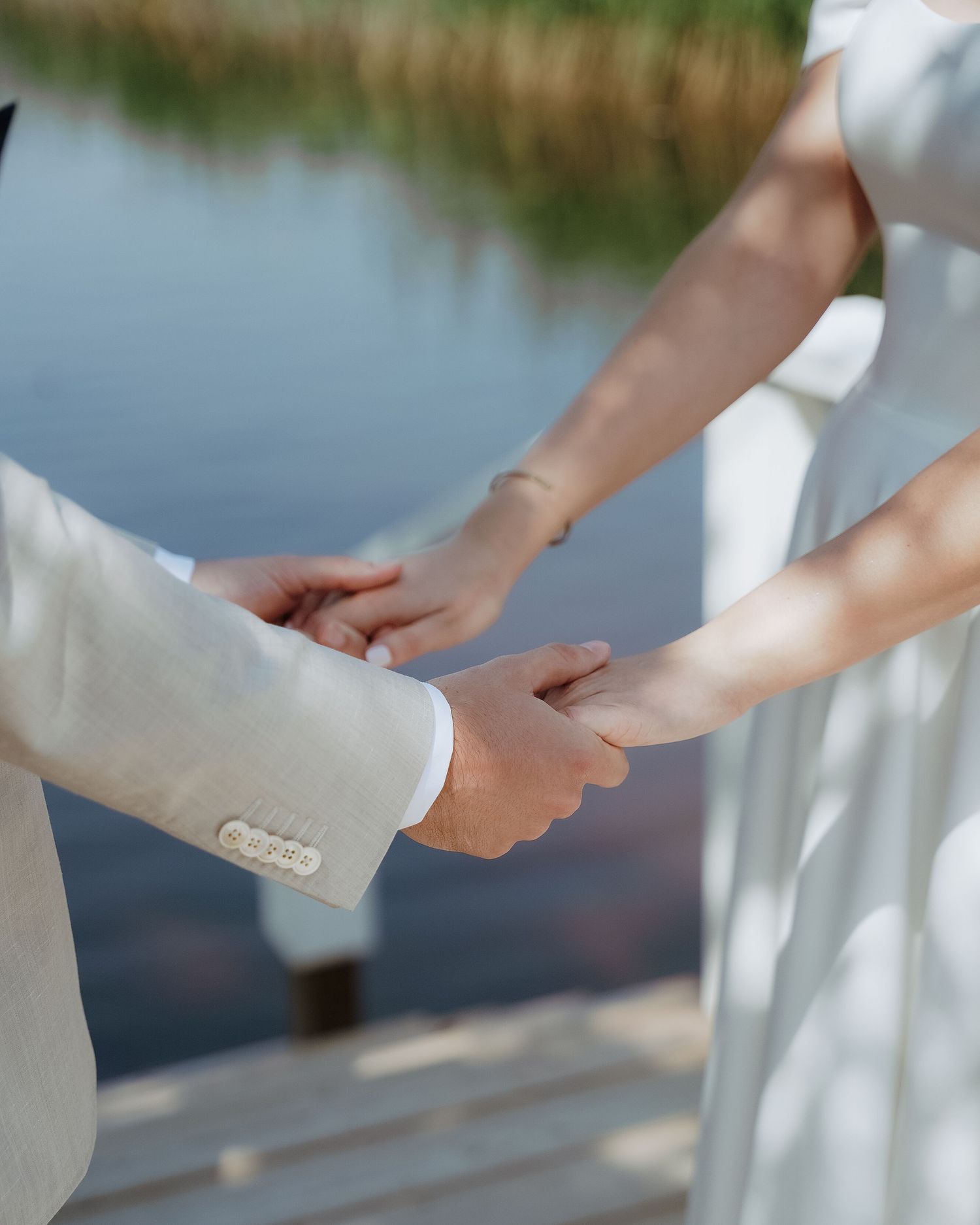 Close-up shot of wedding couple holding hands against a scenic lake backdrop.