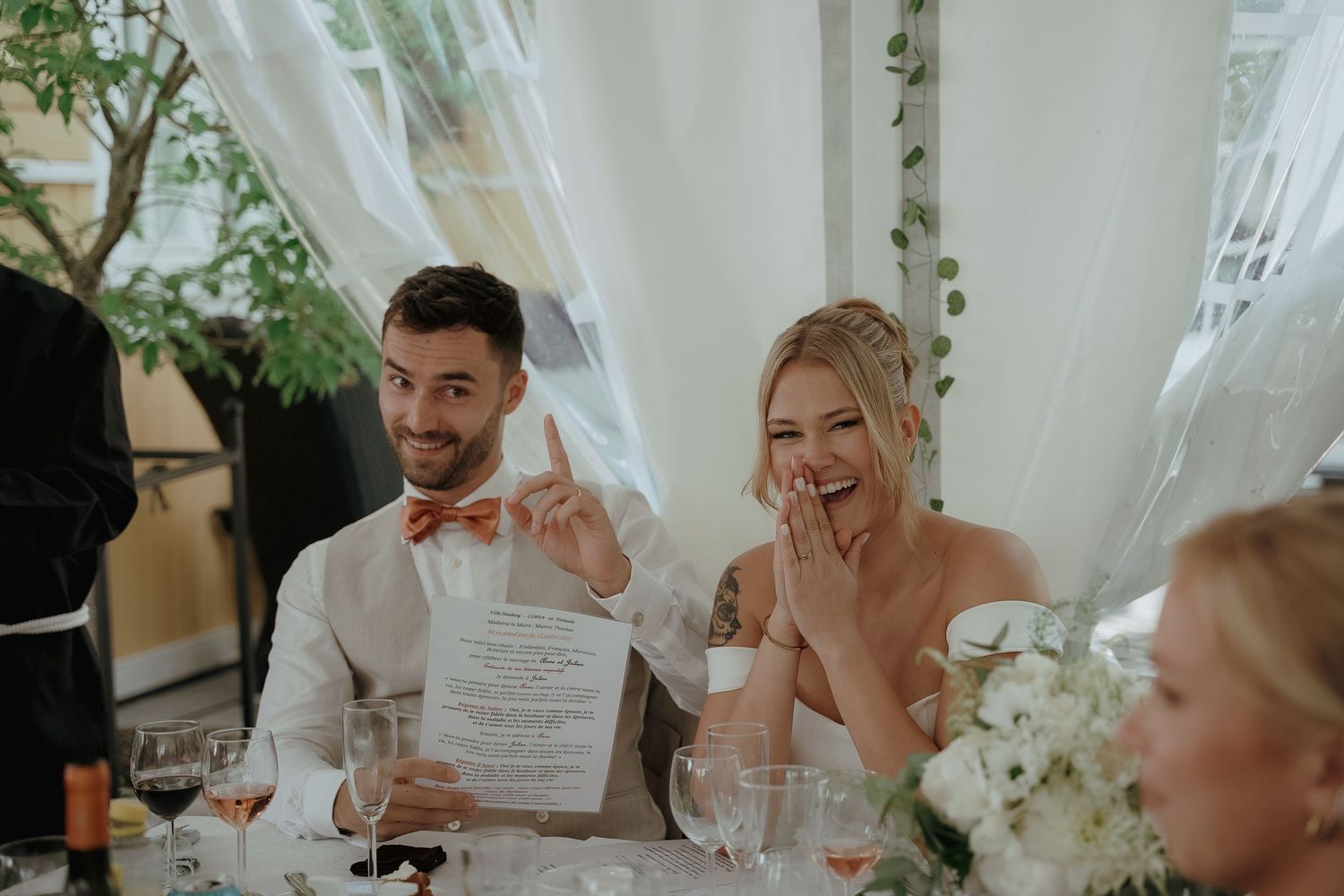 A couple shares a happy moment during their wedding reception at a table decorated with white flowers and drapes.
