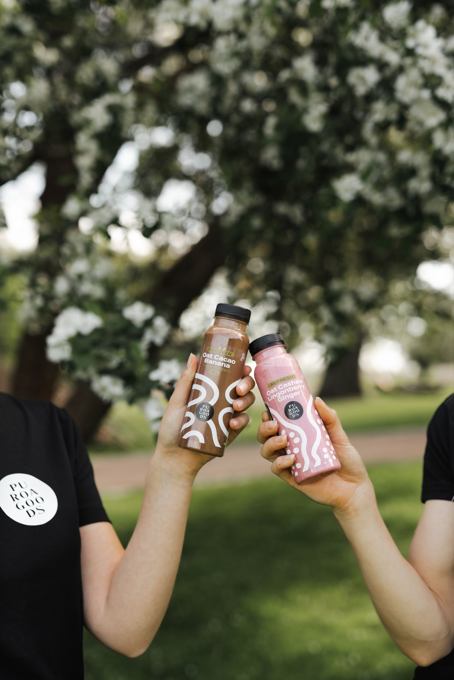 Two hands holding up colorful drink bottles against blurred garden background.