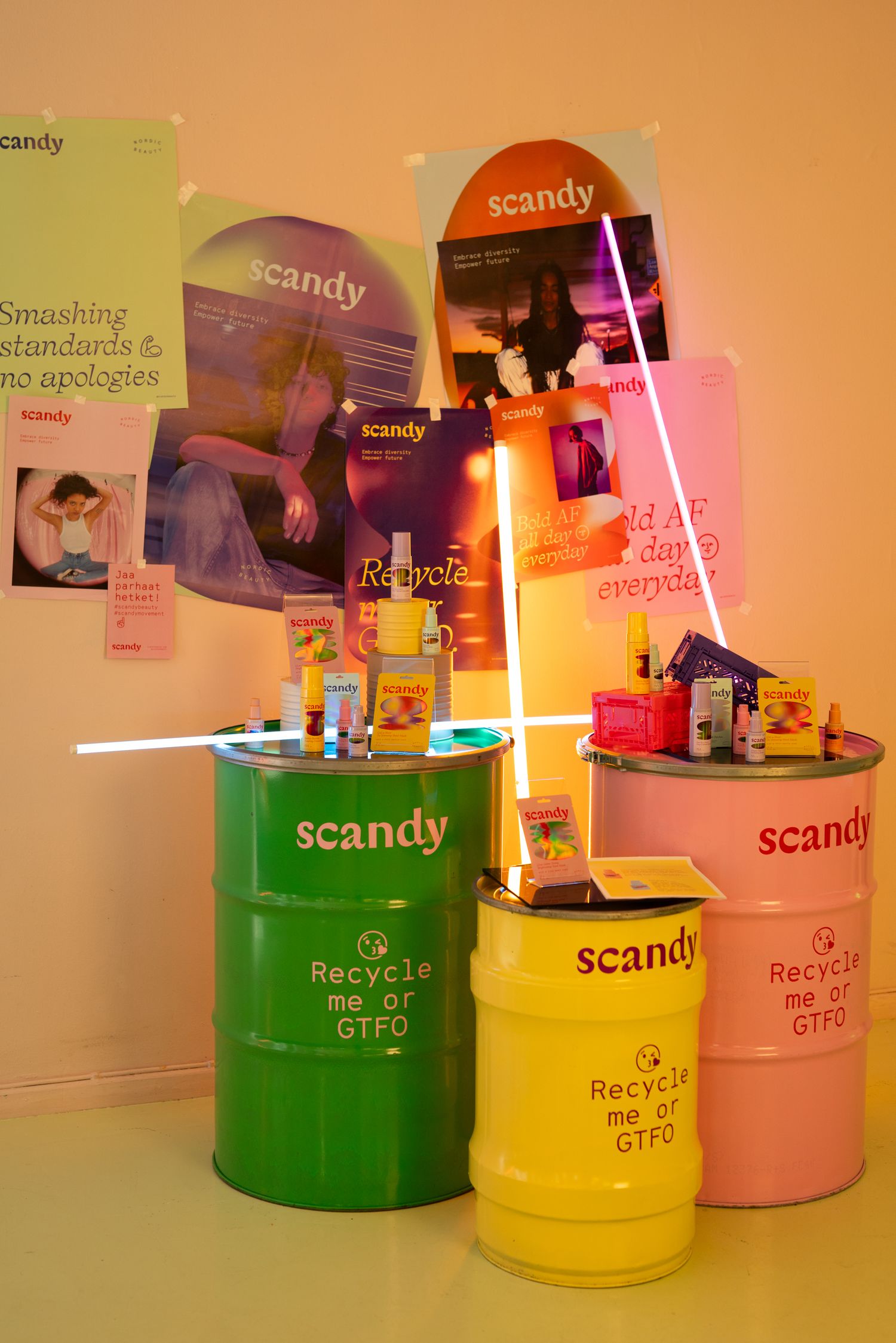 Colorful recycling barrels decorated with Scandy brand posters and neon light tubes in retail display setup.