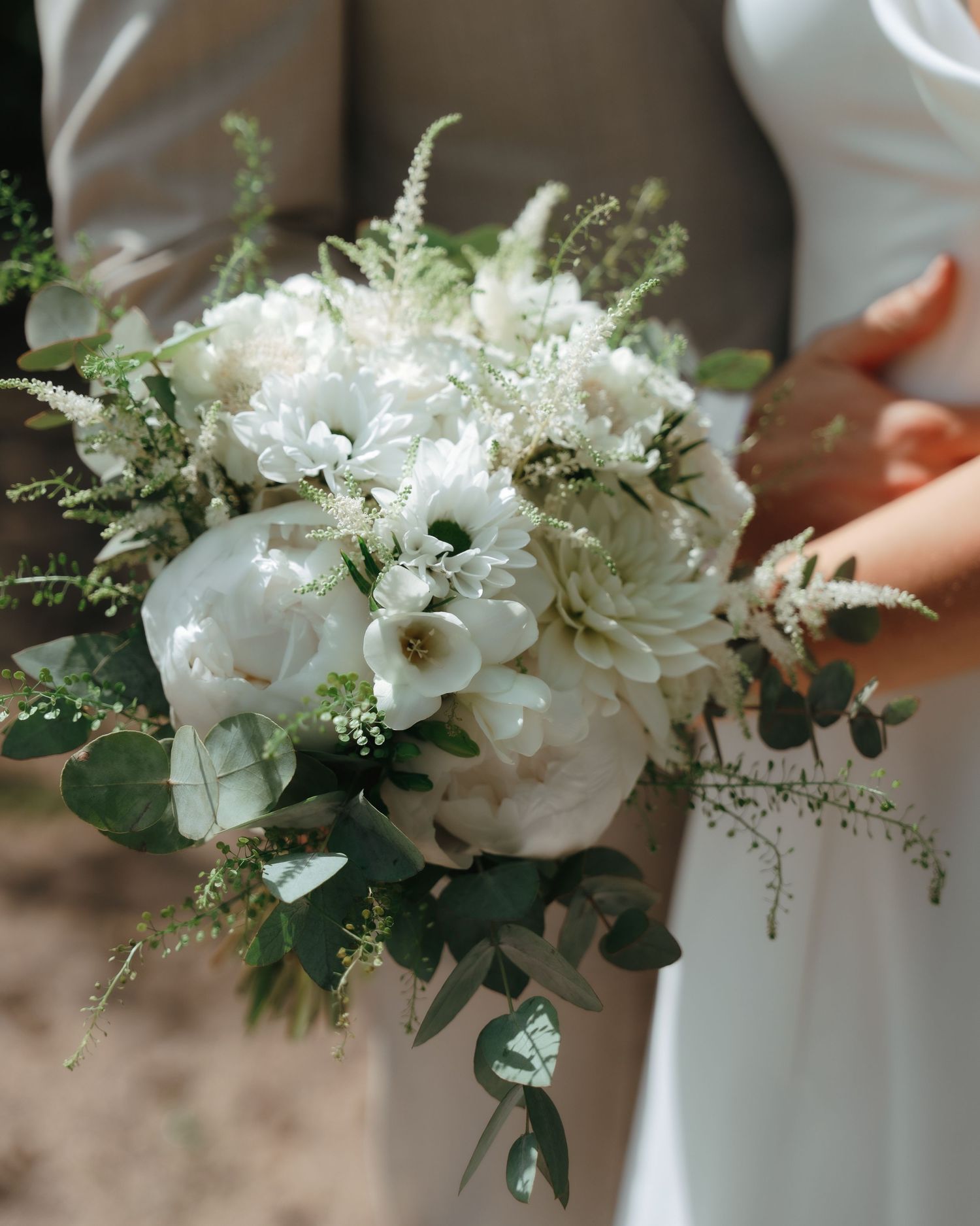 White floral bouquet with eucalyptus greenery against a blurred neutral background.