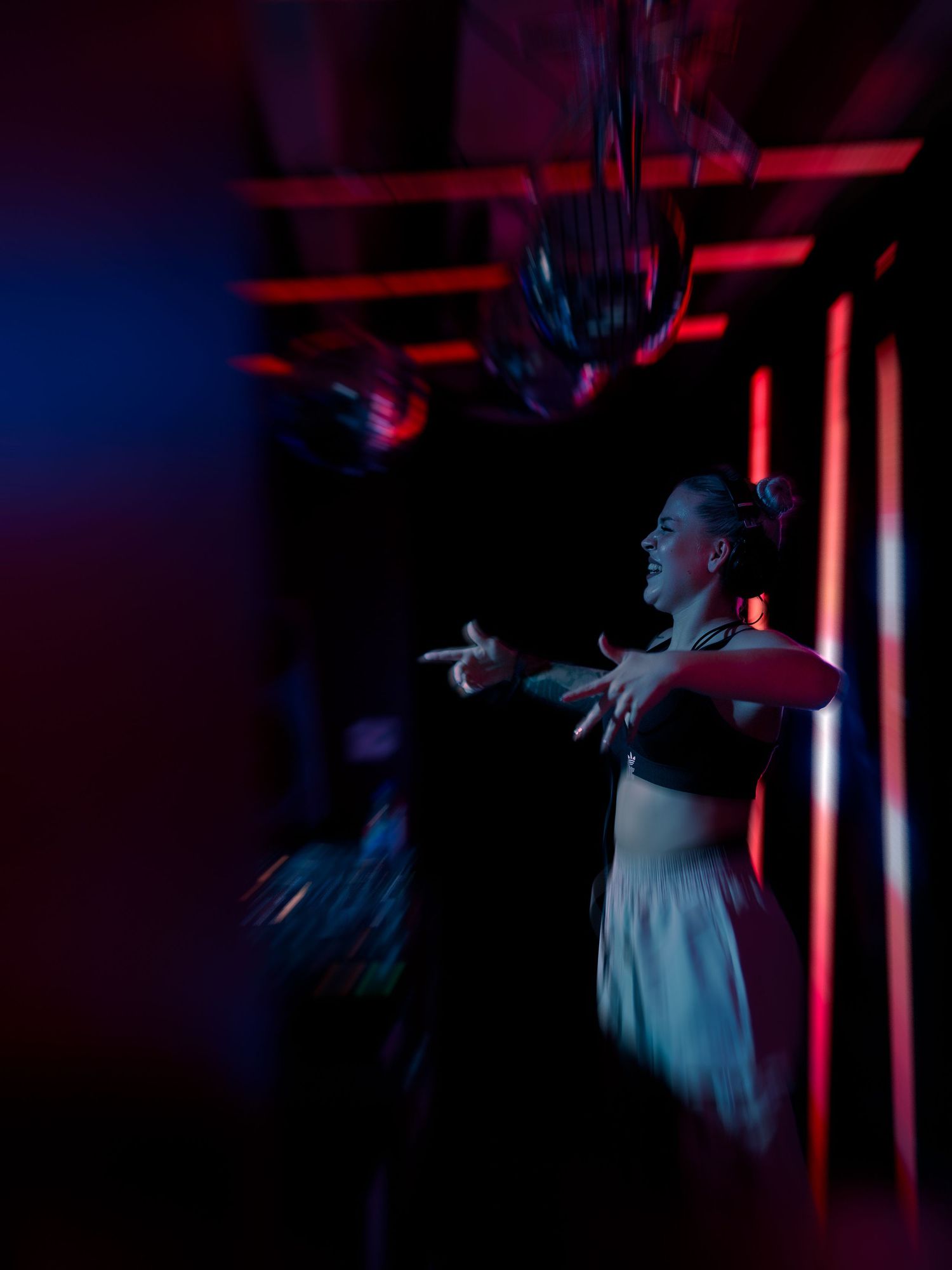 A dancer performs in dramatic red and blue lighting on a dimly lit stage with arms outstretched in a white costume.