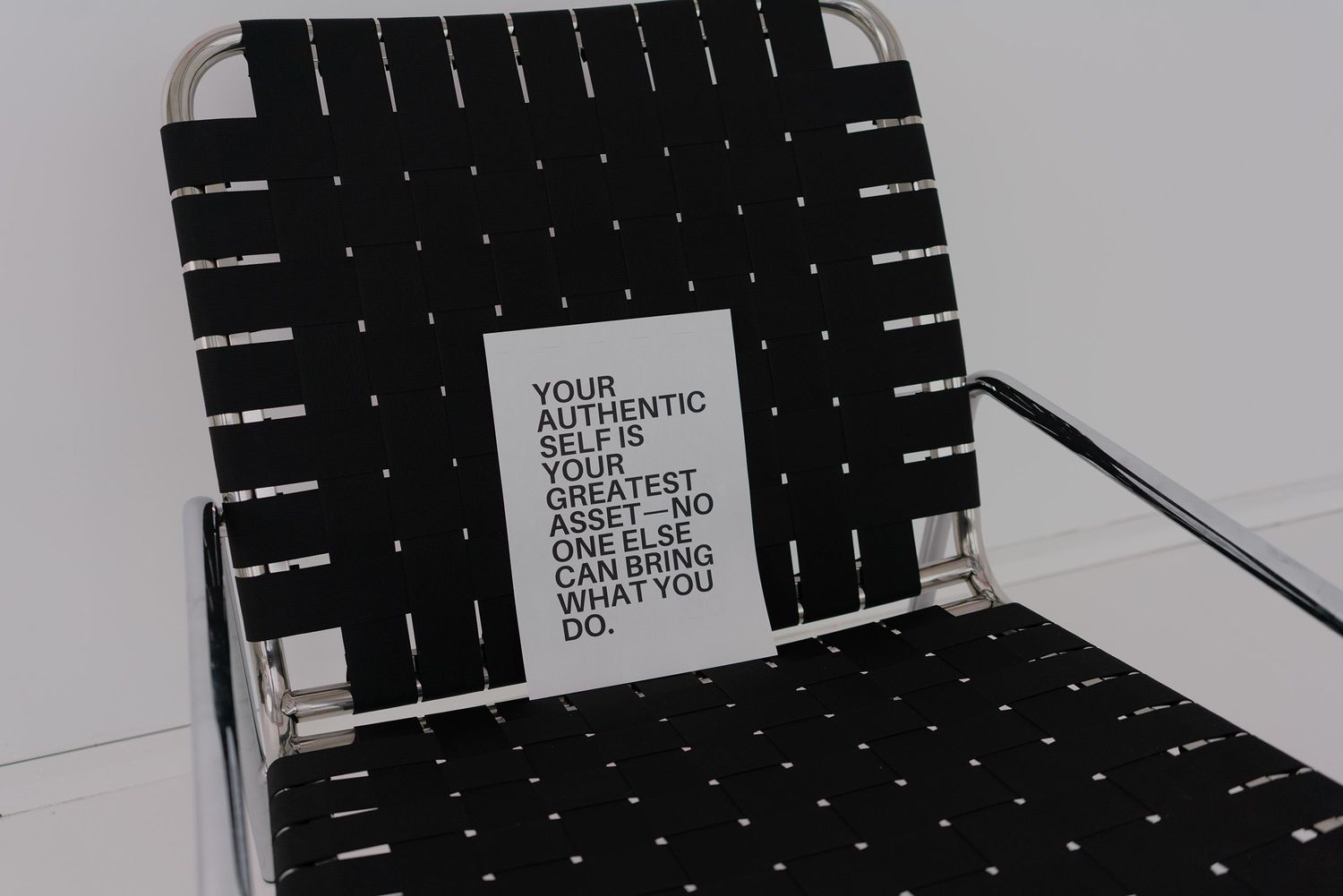 A black and white woven chair holds a text message card in a minimalist setting.