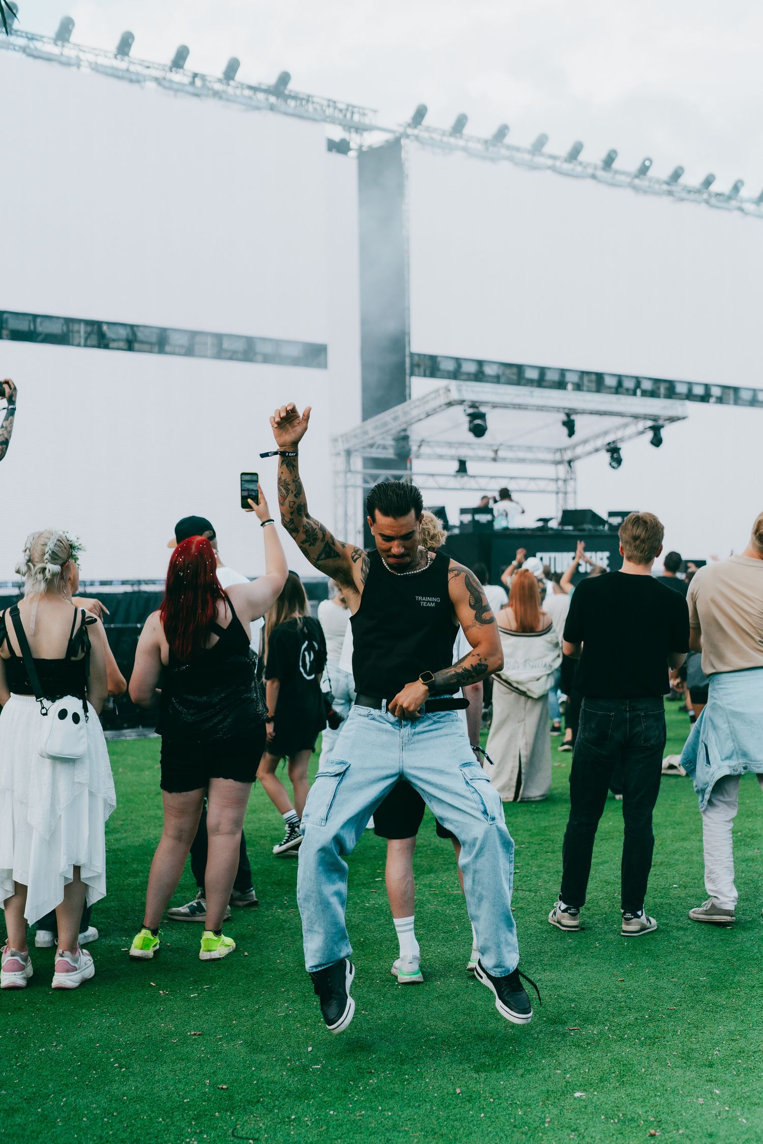 People dancing and celebrating at an outdoor event with white canopy structures and artificial turf flooring.