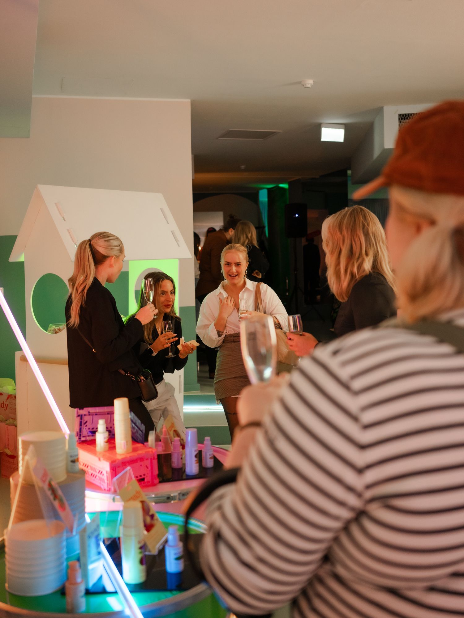 A group of people gather around a bar with colorful neon lighting in an indoor event space.