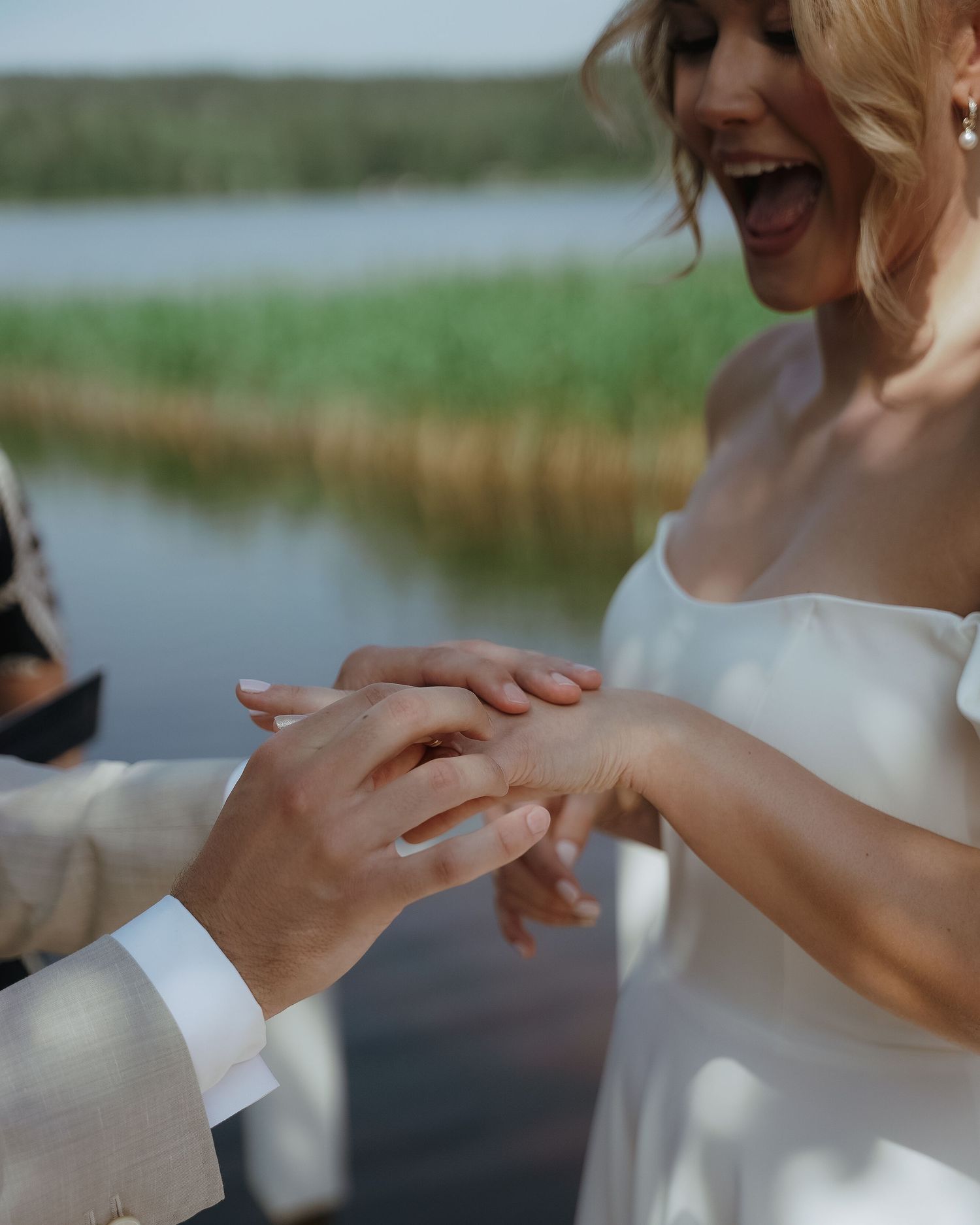 A joyful moment during an outdoor wedding ceremony as a ring is placed on a finger by a lake.