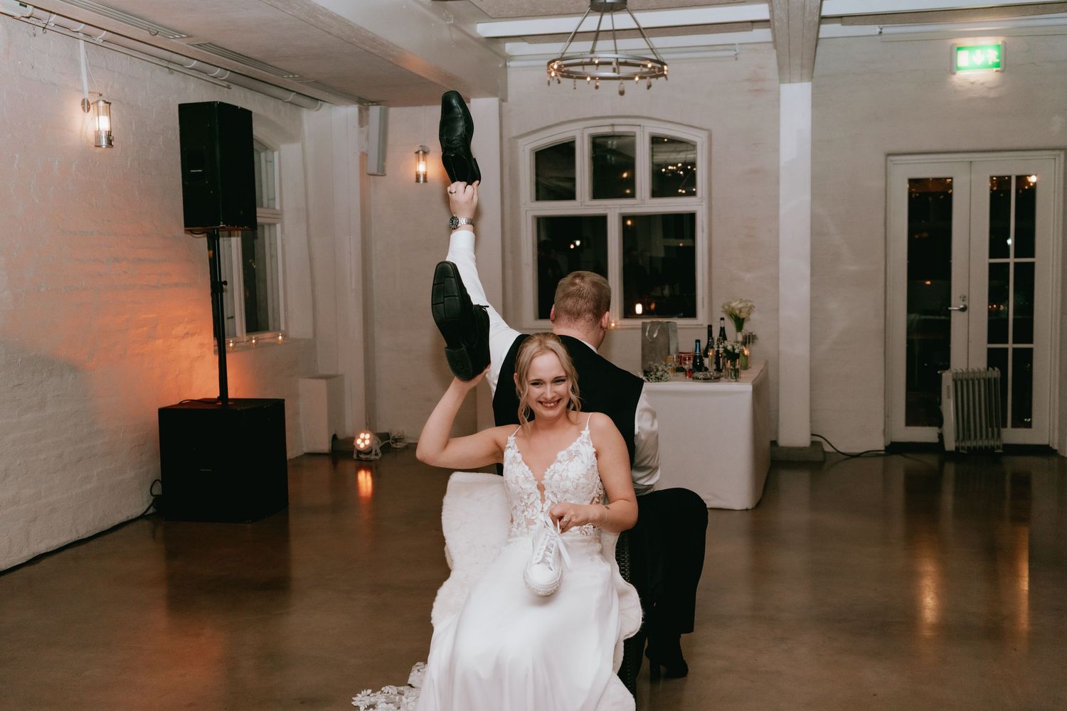A joyful wedding celebration moment where someone in a white dress dances surrounded by party guests at an indoor venue.