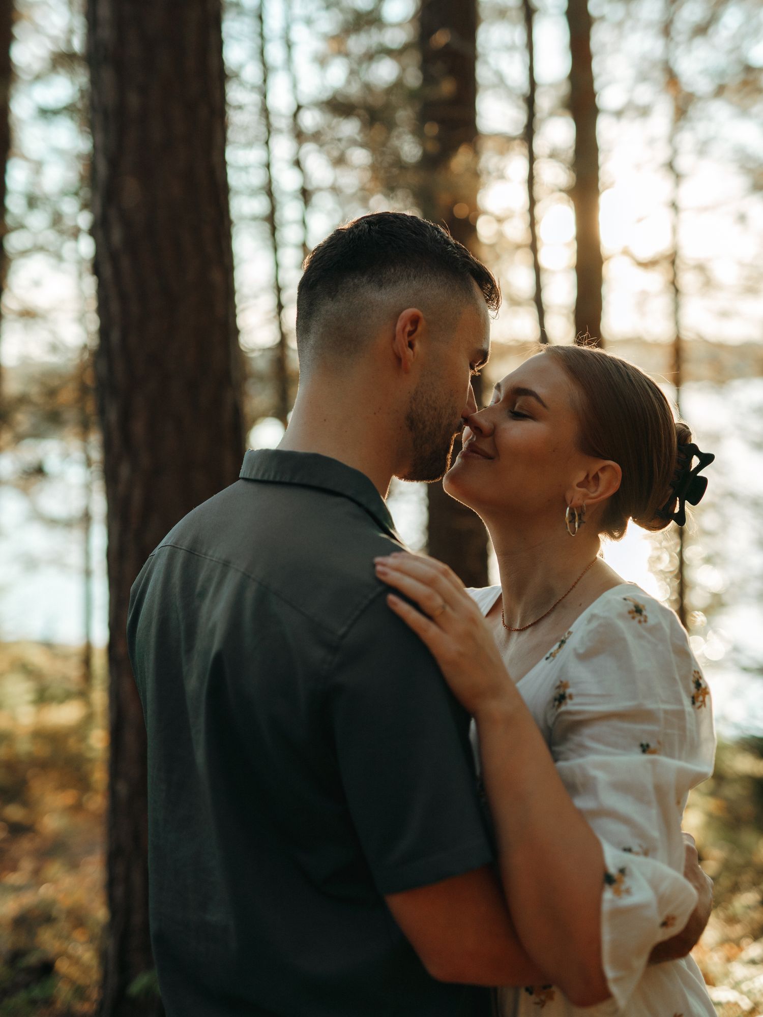 Romantic couple sharing a tender kiss in a sunlit forest setting with golden light filtering through the trees.