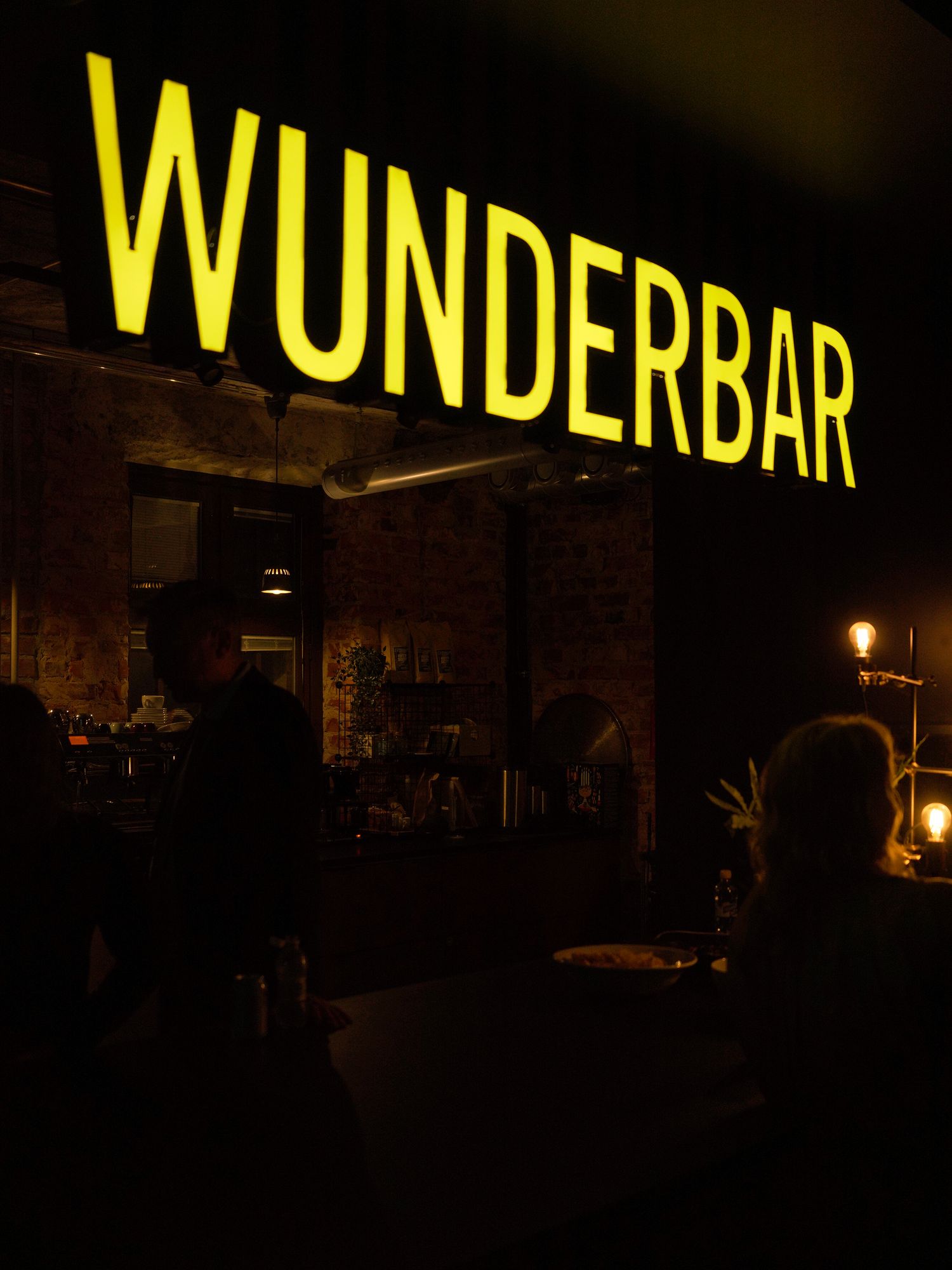 Wunderbar illuminated yellow sign glowing in a dark atmospheric bar with brick walls and dim lighting.