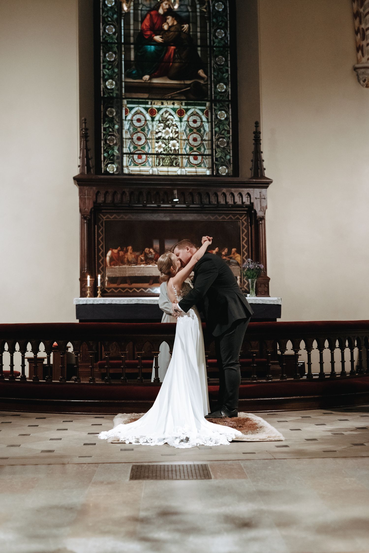 Couple shares romantic moment in vintage church with stained glass windows and ornate wooden altar decoration.