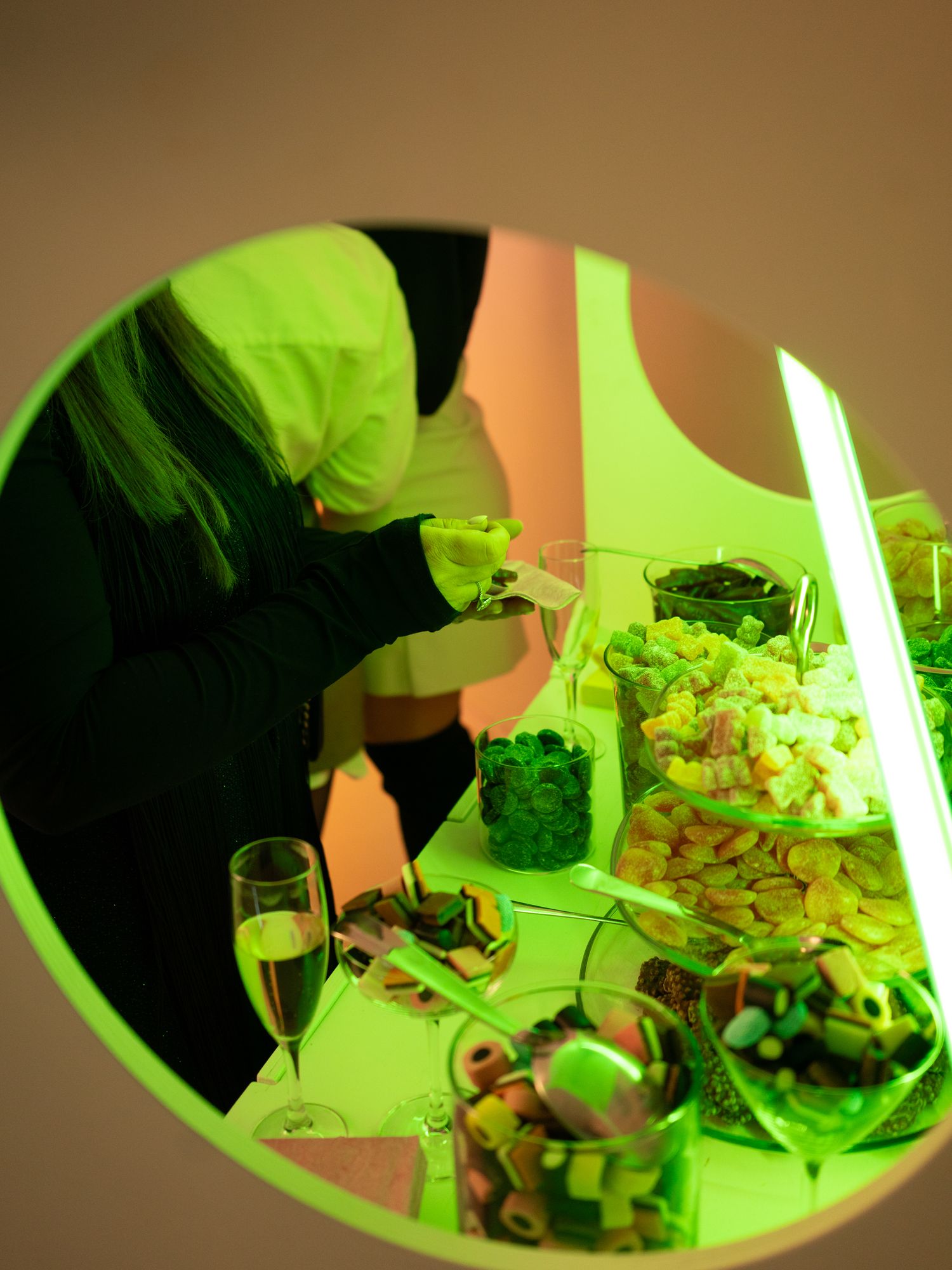 A person serving appetizers and drinks at a party table with green lighting illuminating the snacks and glassware.