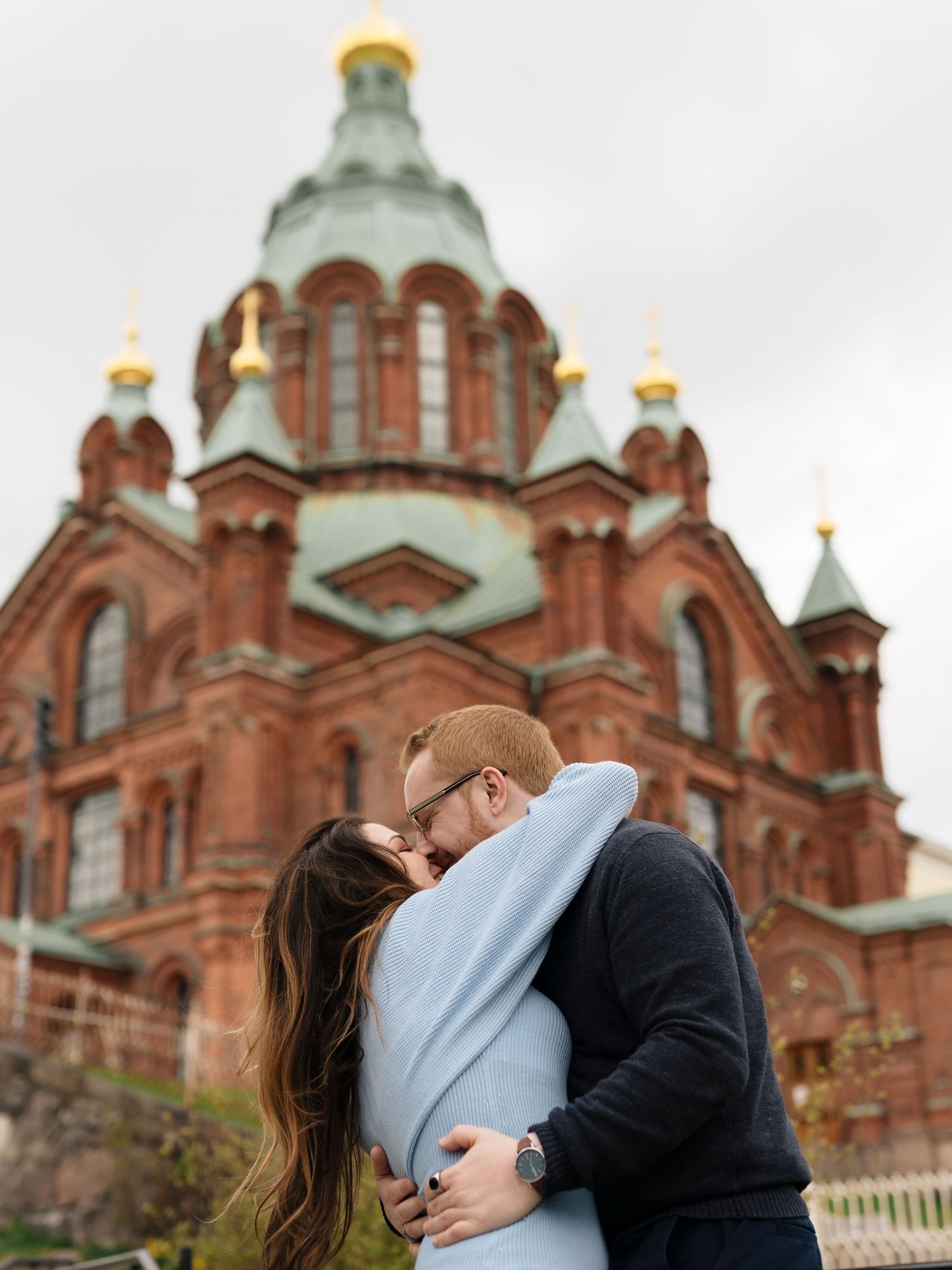 Couple sharing a romantic kiss in front of the Uspenski Cathedral in Helsinki, Finland.