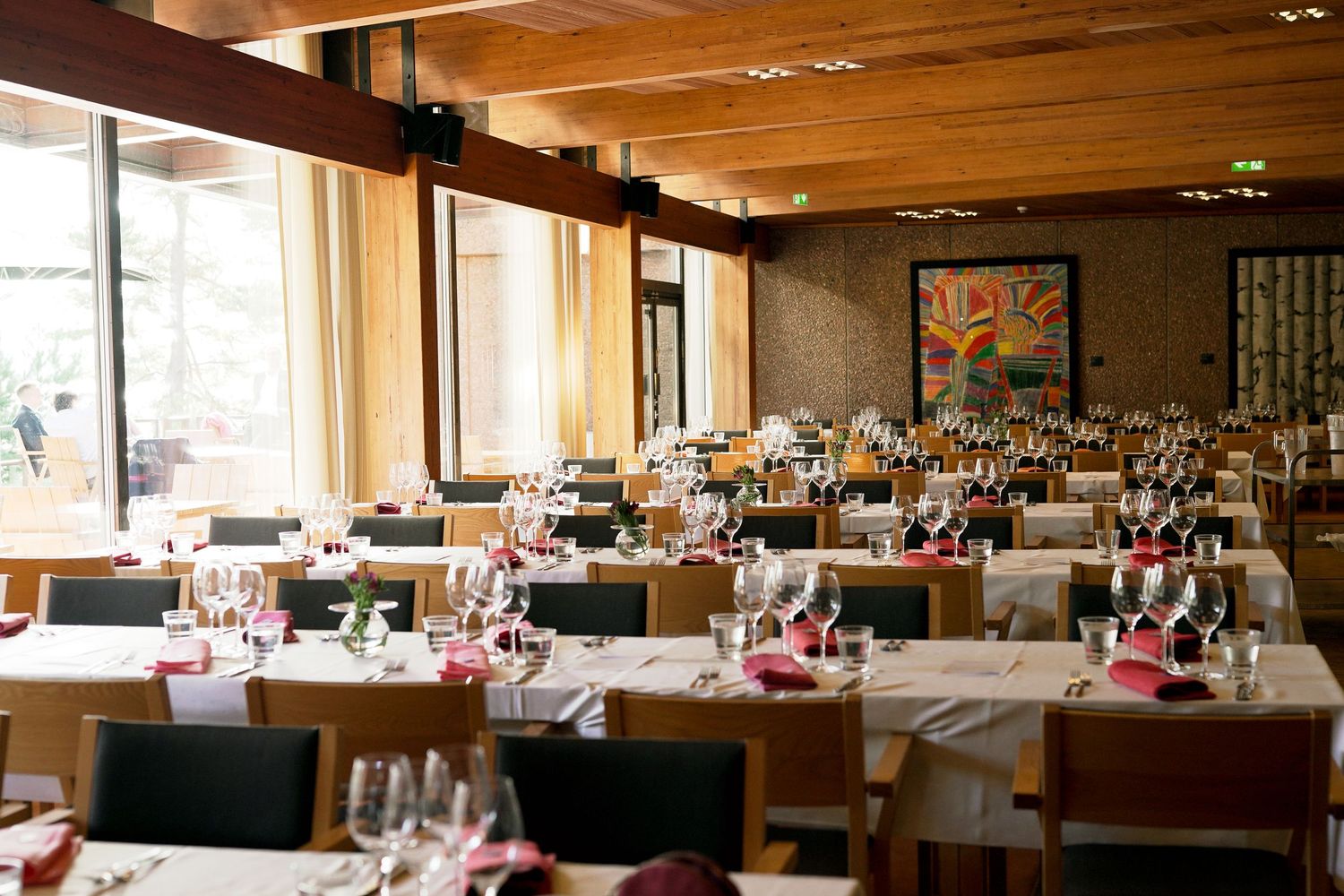 Elegant restaurant dining room with white tablecloths, wine glasses, wooden ceiling, and colorful artwork on the wall.