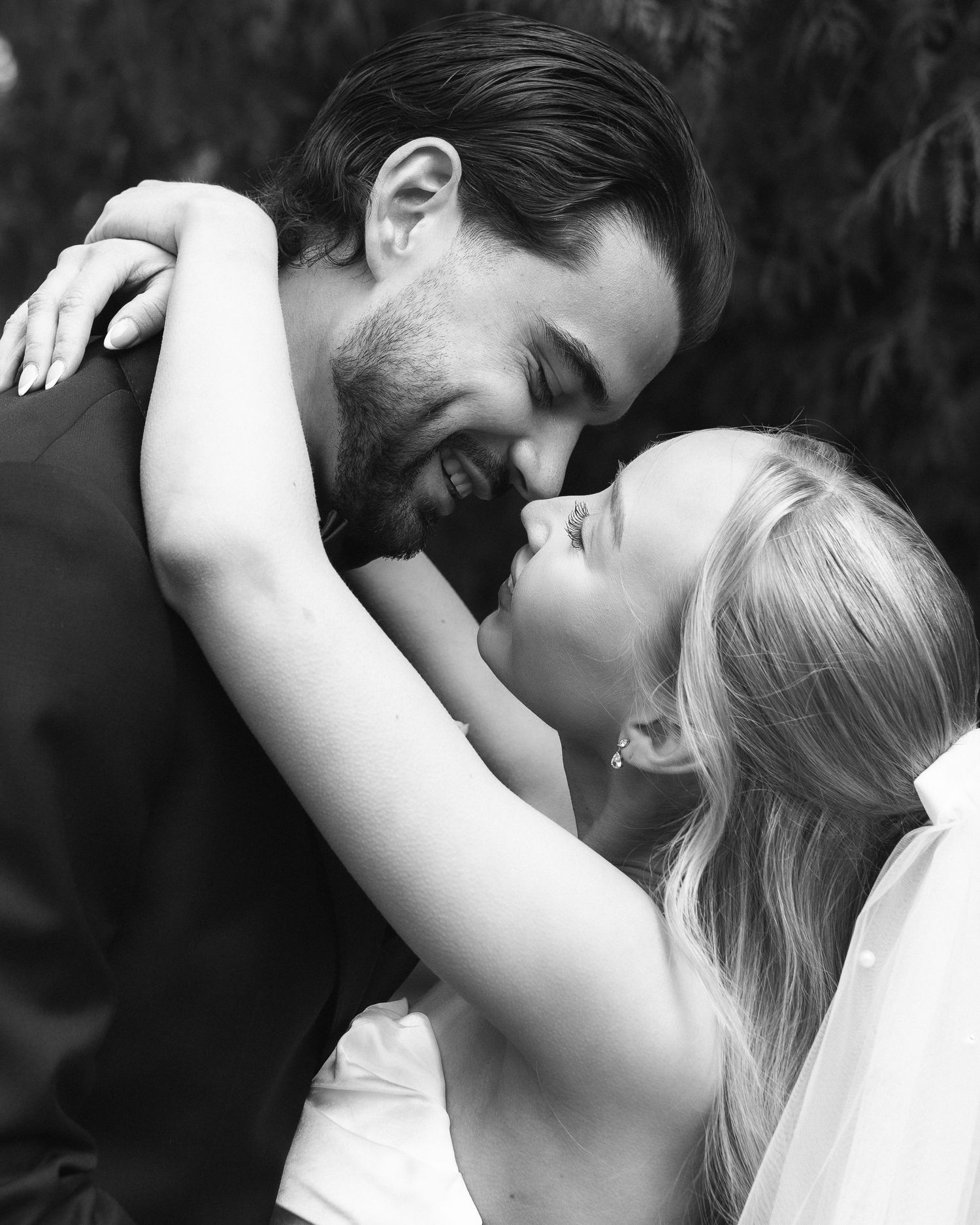 Black and white wedding photo of bride and groom sharing a romantic moment, noses touching and smiling.