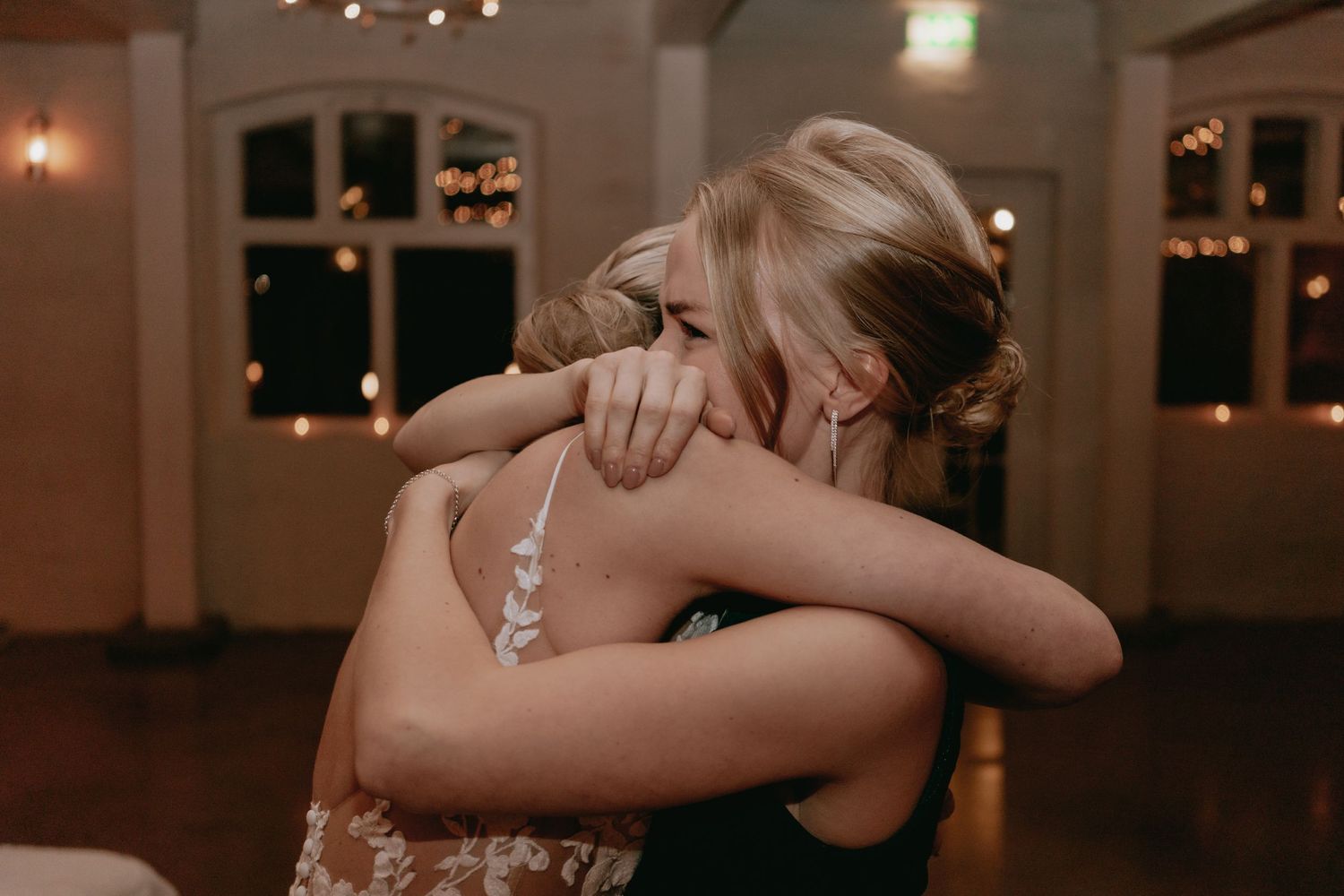 Two people share an emotional embrace on a dimly lit dance floor during what appears to be a special celebration.