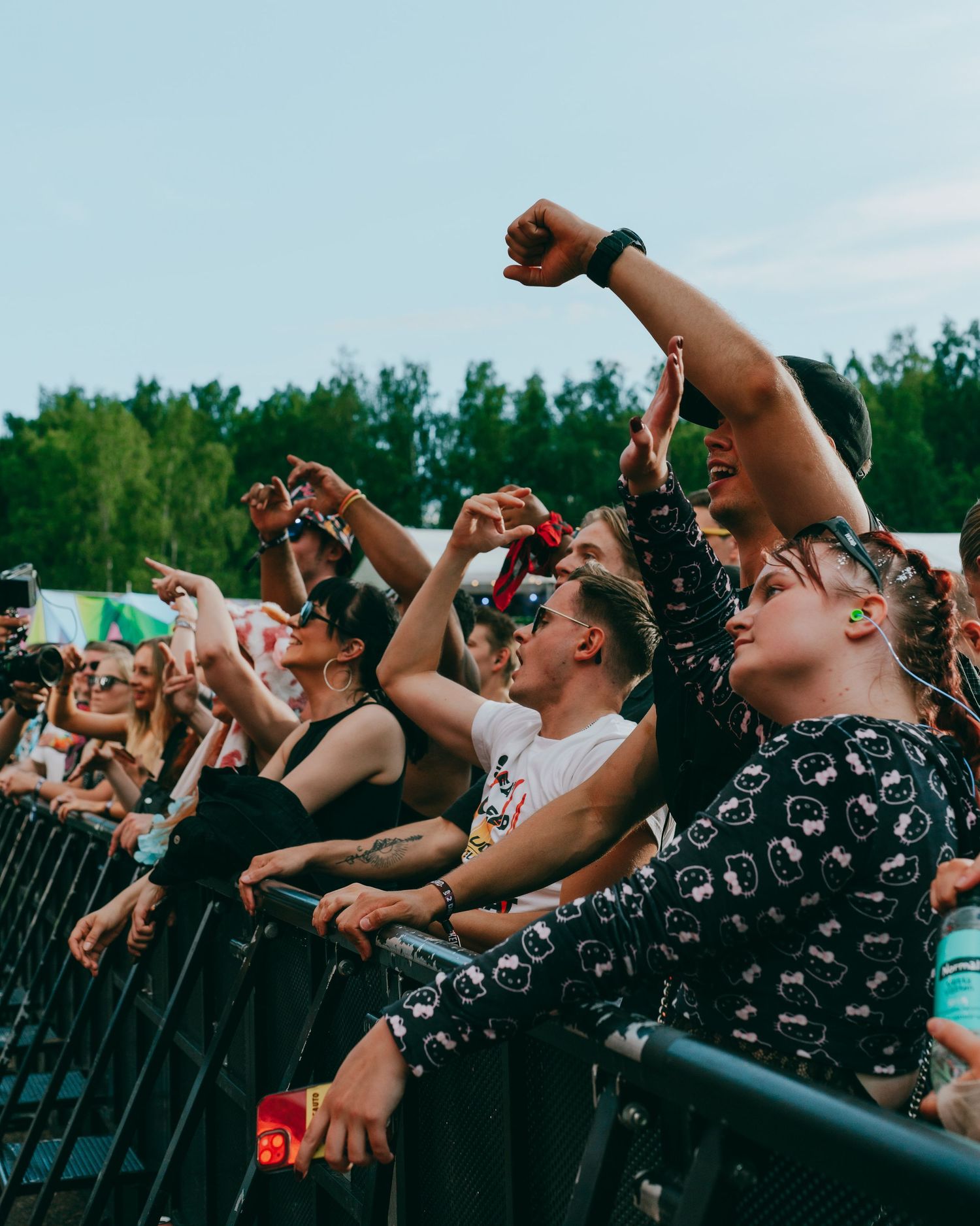Enthusiastic music festival crowd singing and cheering with raised arms against a backdrop of trees during an outdoor concert.
