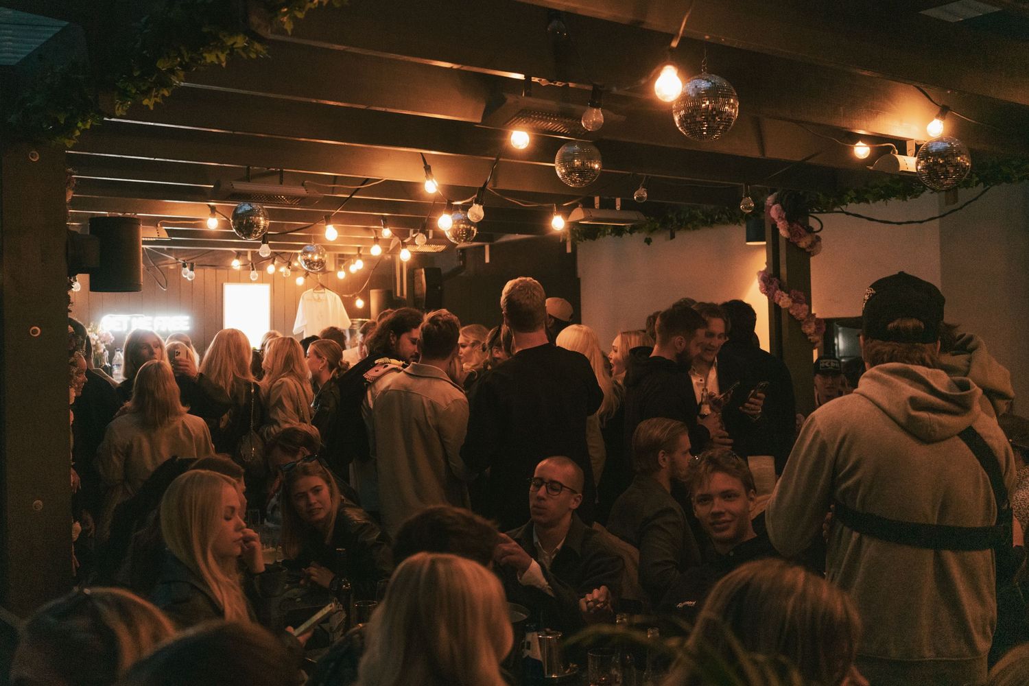 A crowded dimly lit basement bar or venue filled with people socializing under warm overhead lighting.