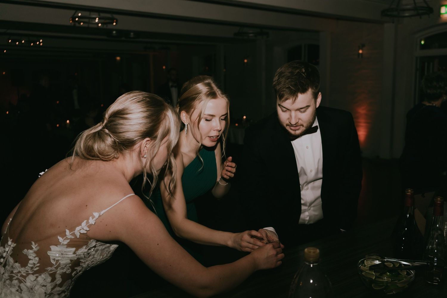 A group of formal party guests huddle close together in conversation at an elegant dimly lit evening event.