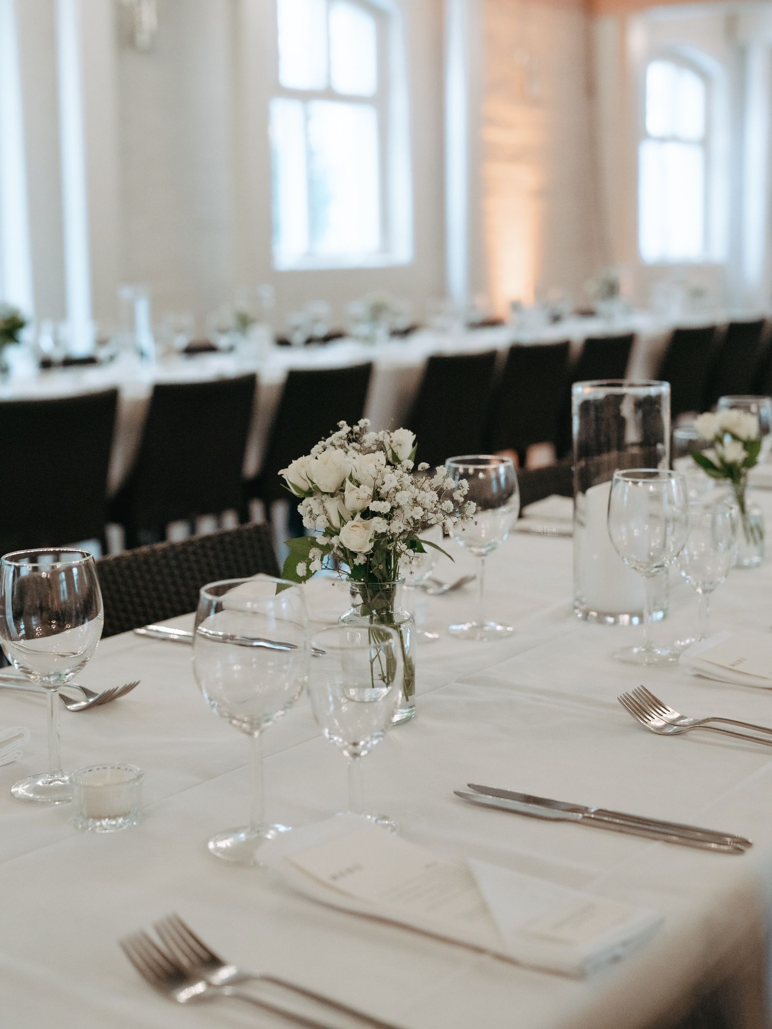 Elegant wedding reception table setting with white tablecloth, crystal glassware and delicate white rose centerpieces.