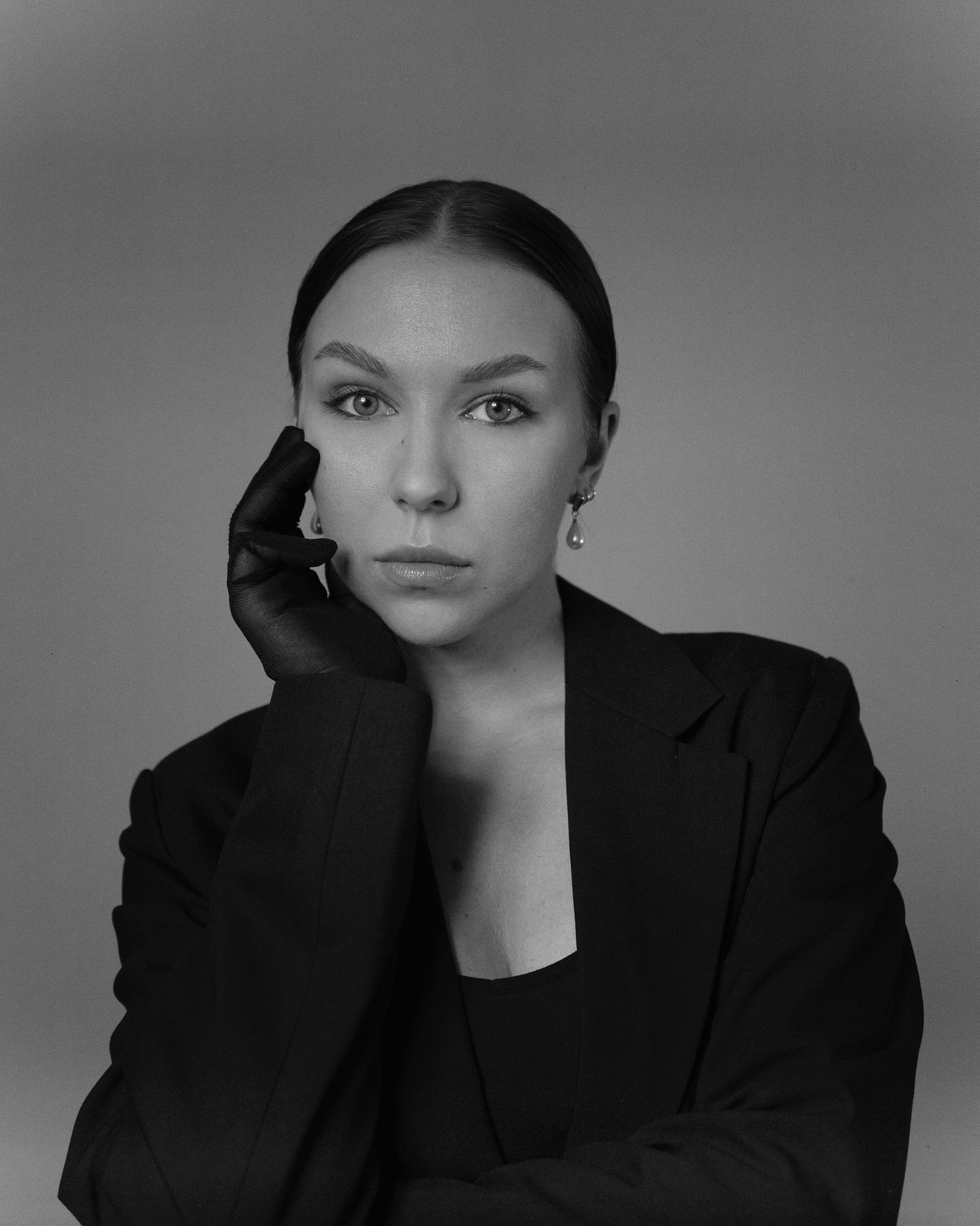 Black and white studio portrait of someone in a dark blazer posing elegantly against a neutral background.
