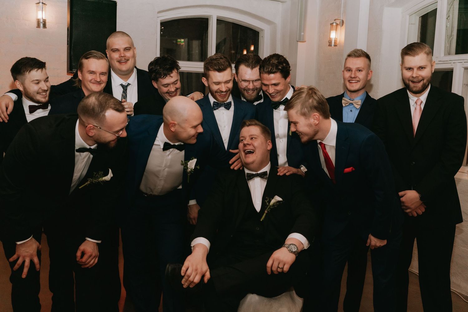 A group of men in formal tuxedos and suits share a candid laughing moment at an elegant event.