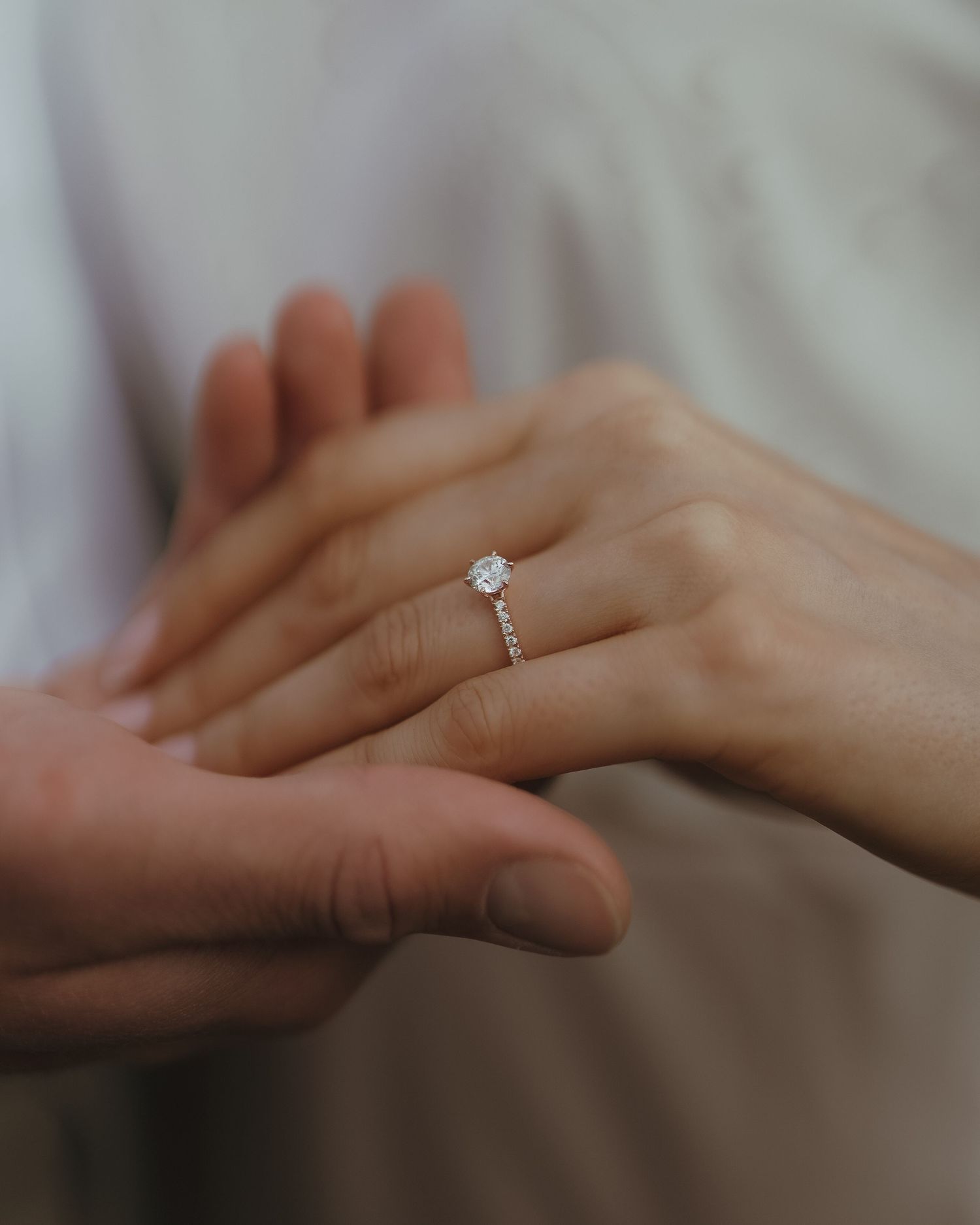 A delicate engagement ring with a solitaire diamond sparkles as two hands touch in an intimate moment.