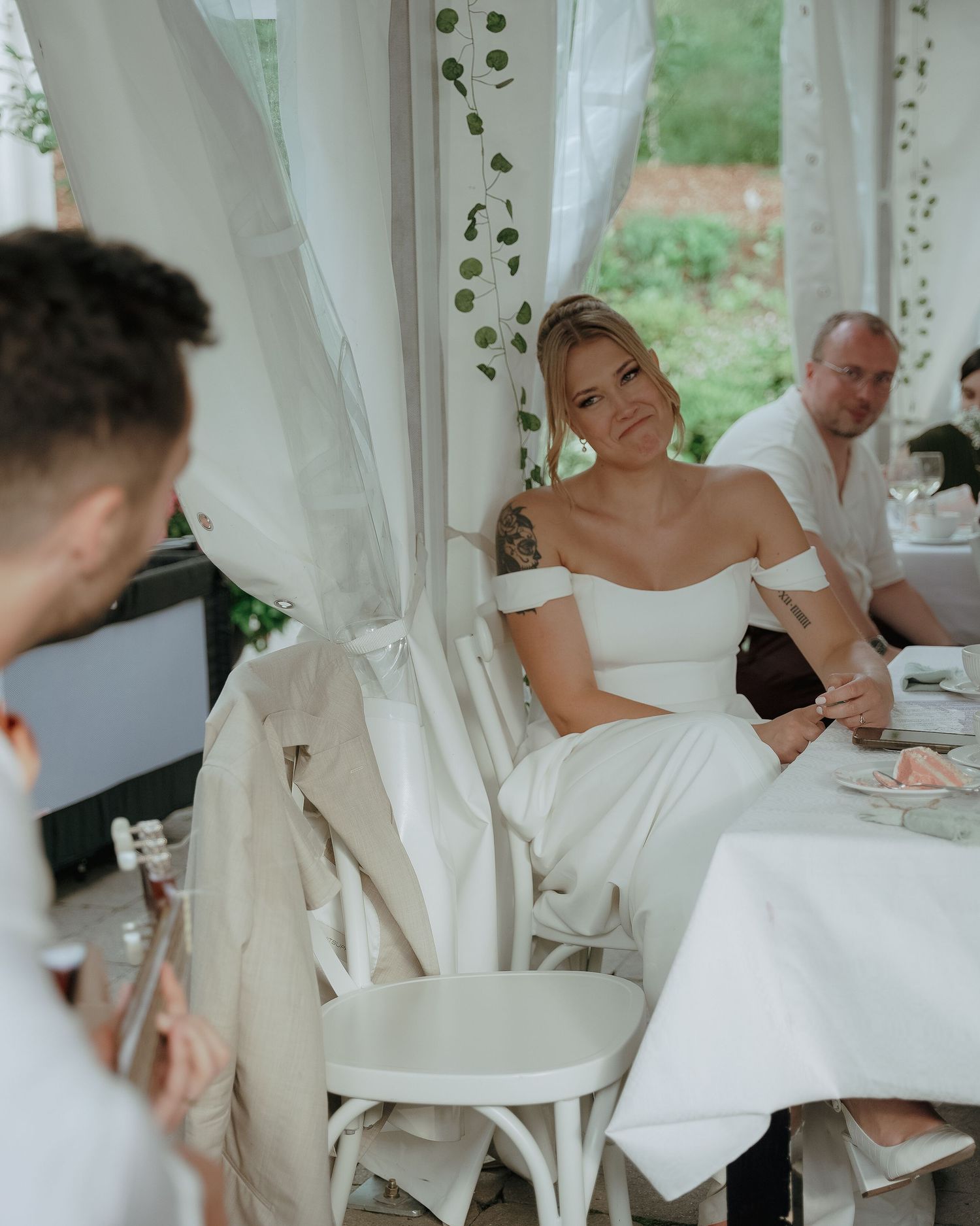 People gathered at an elegant outdoor dining event under white curtains and decor with string lights and greenery.