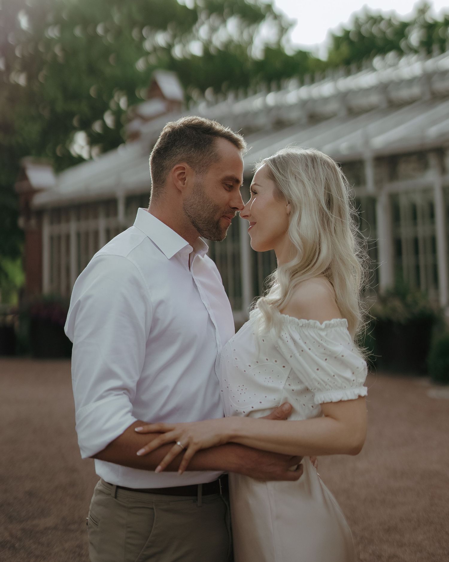 A romantic couple in soft earthy tones dances intimately in an outdoor garden setting during golden hour.