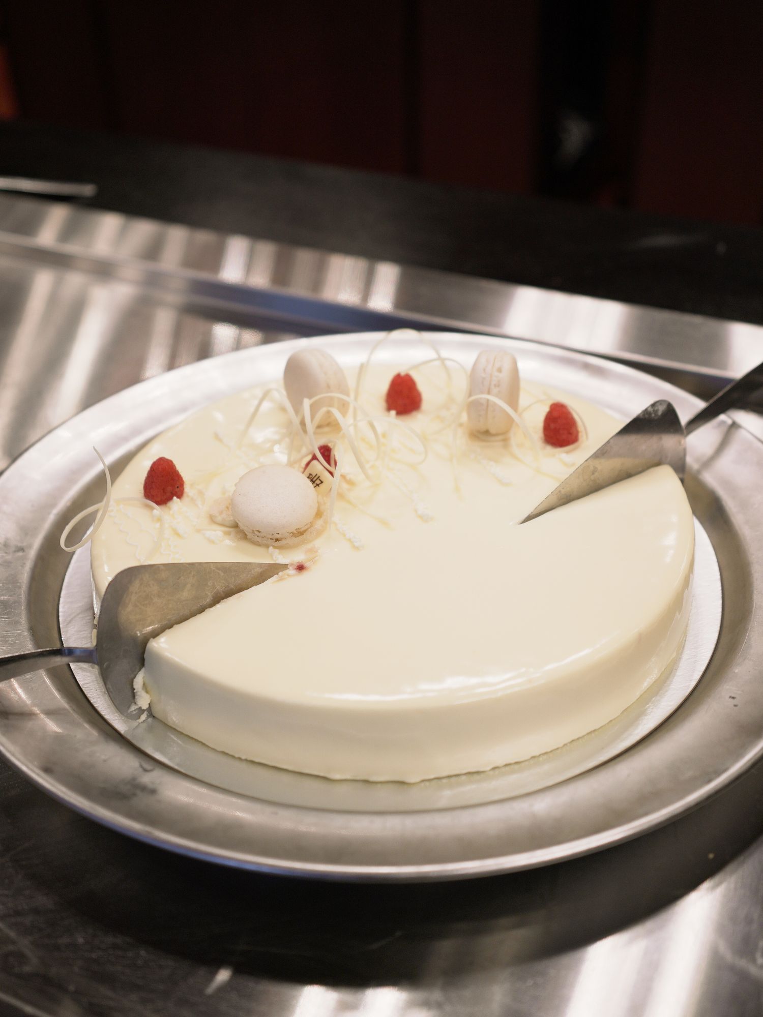 Elegant white mousse cake with strawberry decorations and a slice cut, served on a silver platter.