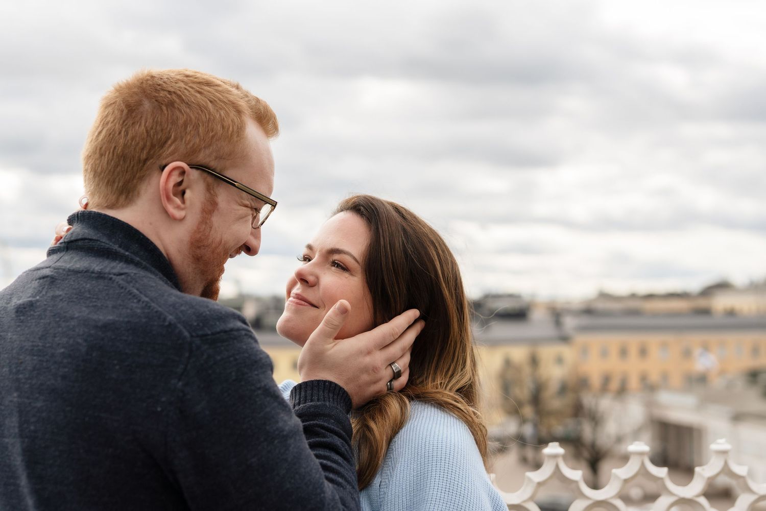 A romantic couple shares a tender moment outdoors, man gently touching womans face while smiling at each other.