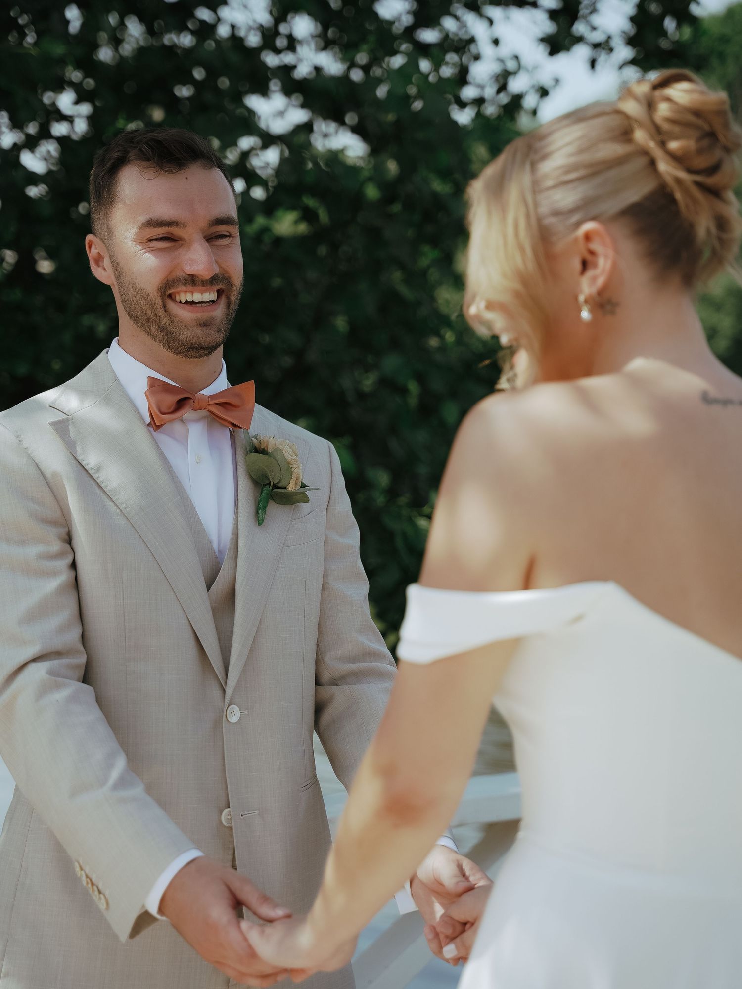 A newlywed couple shares joyful moments during an outdoor wedding ceremony in beige and white attire.