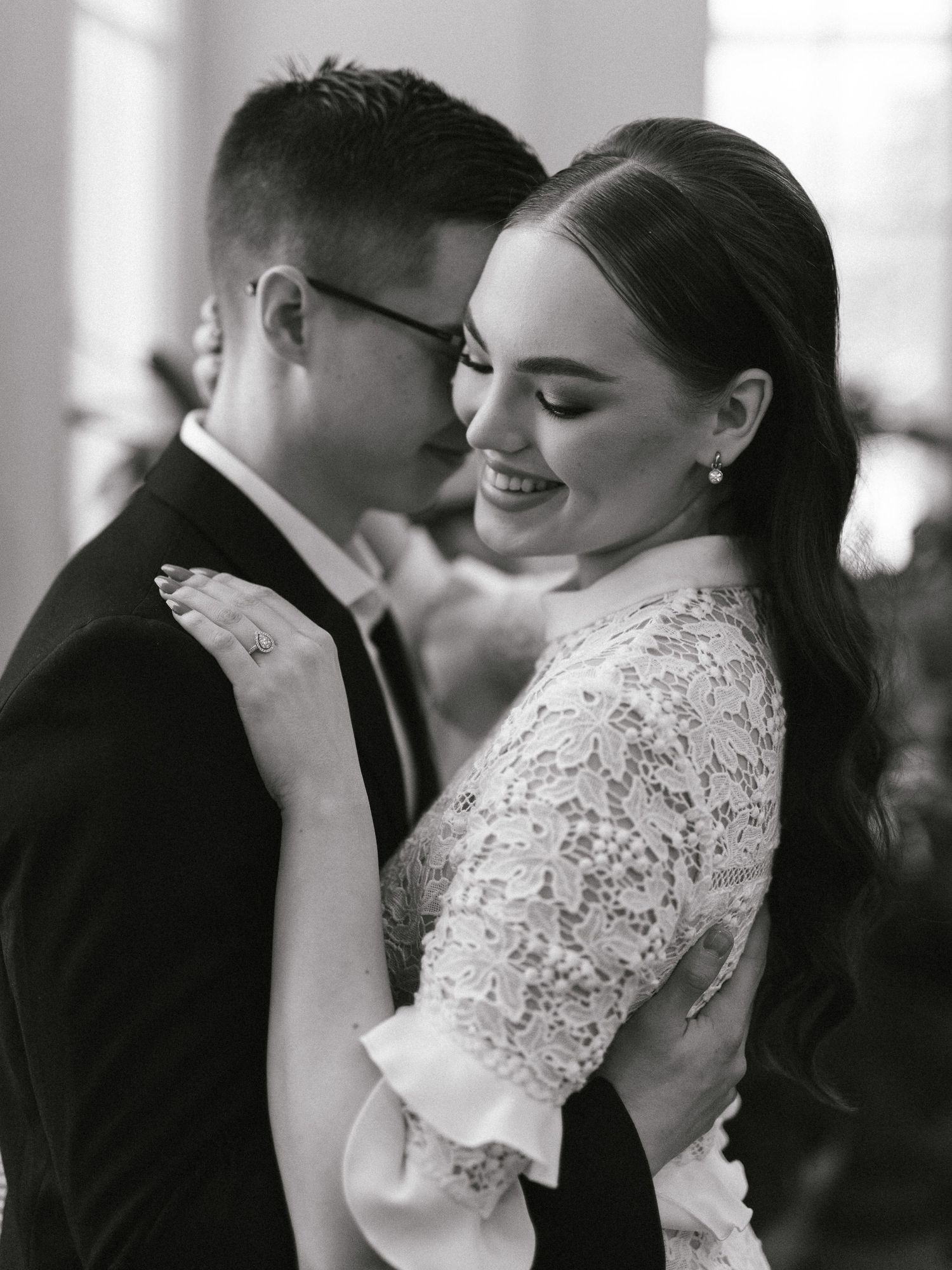 A tender wedding moment captured in black and white showing a couple embracing, with the bride wearing lace and groom in suit.