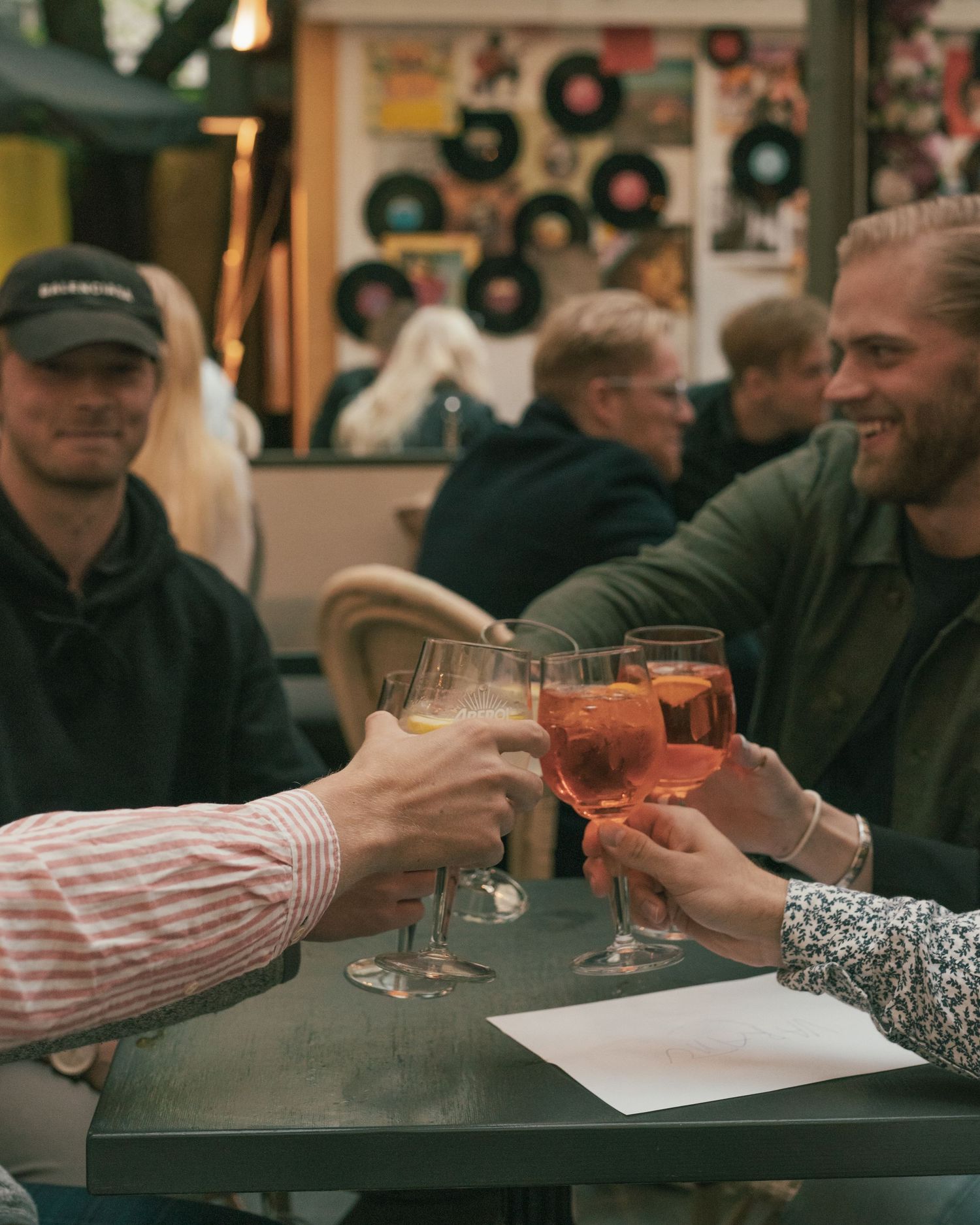 Friends toasting with glasses of wine at a restaurant with vintage vinyl records decorating the wall in background.