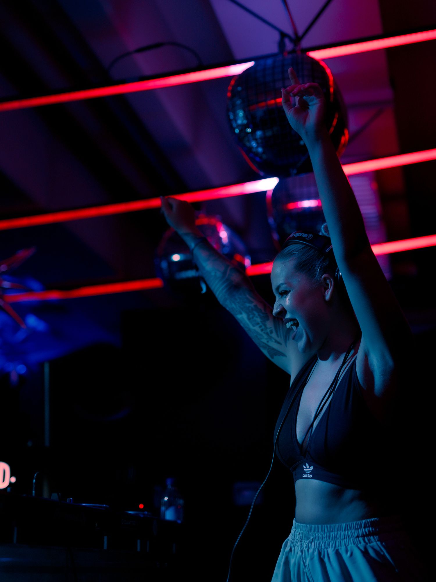 A performer dances energetically under dramatic red and blue lighting in a nightclub setting.