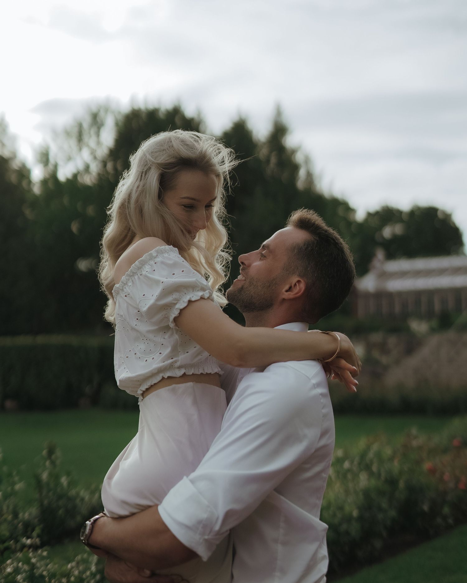 Romantic couple sharing a tender embrace in a garden during golden hour on a cloudy day.