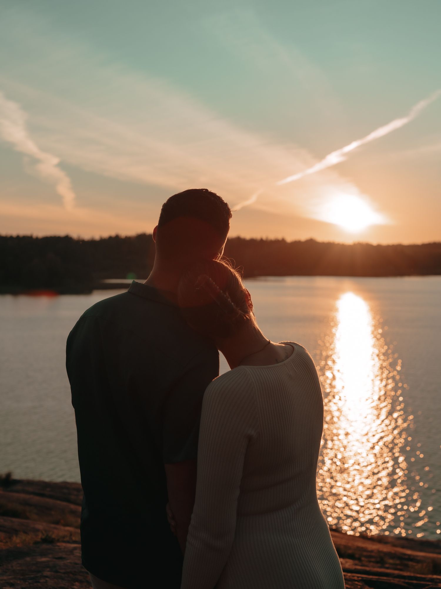 Silhouetted couple watches vibrant sunset over a tranquil lake with shimmering water reflections.