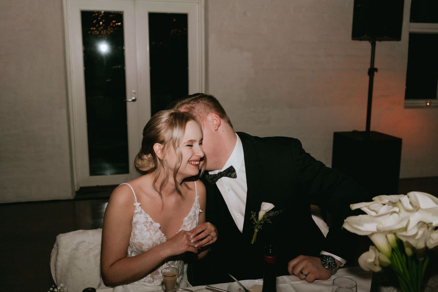 At an elegant wedding reception, a couple shares an intimate moment while seated at their dining table.