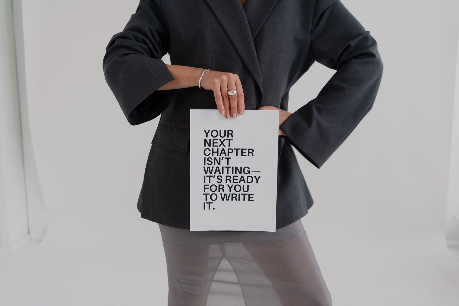 A person wearing a dark blazer holds up a white page with black minimalist typography against a light background.
