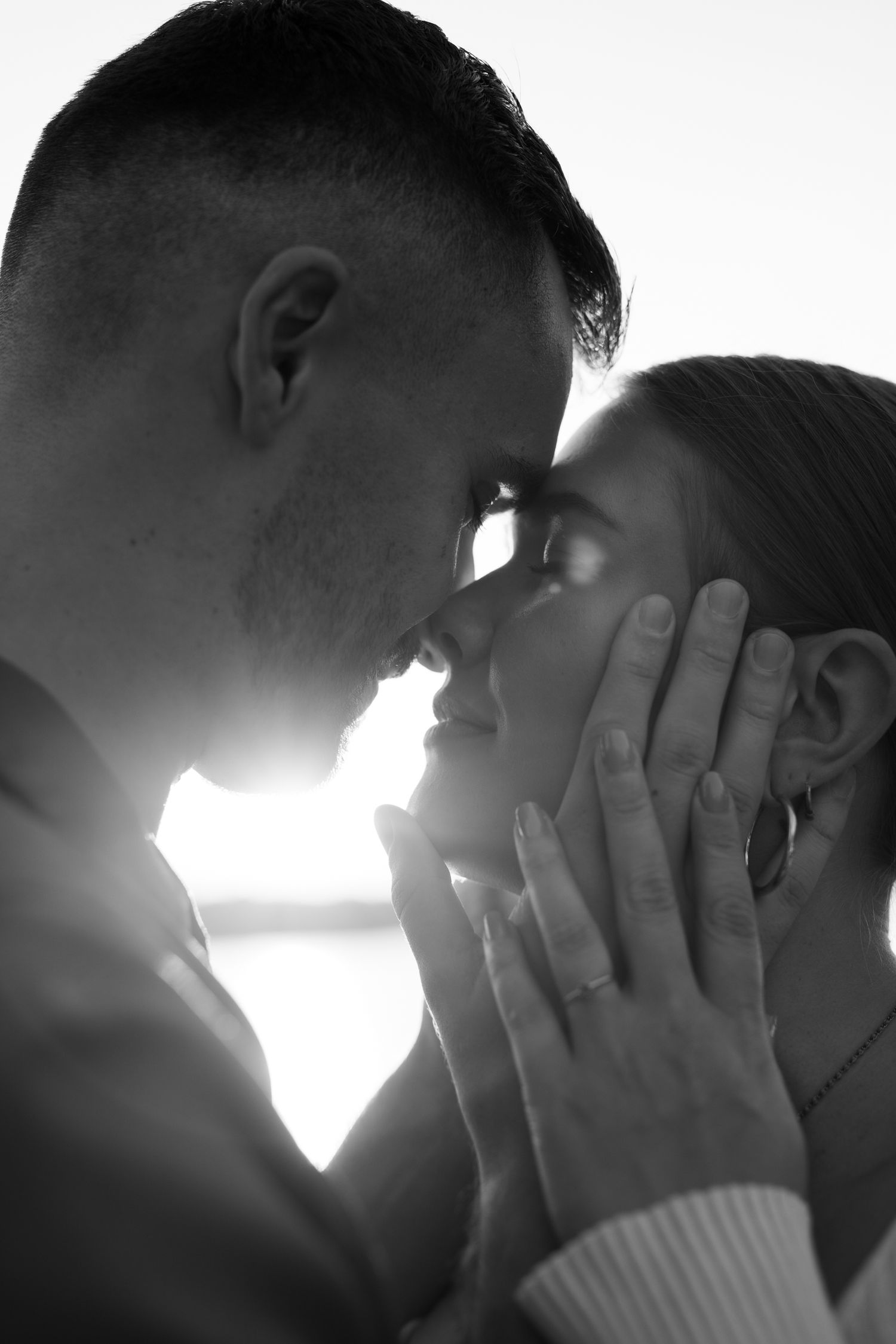 A romantic black and white silhouette of a couple touching foreheads tenderly in soft backlight.