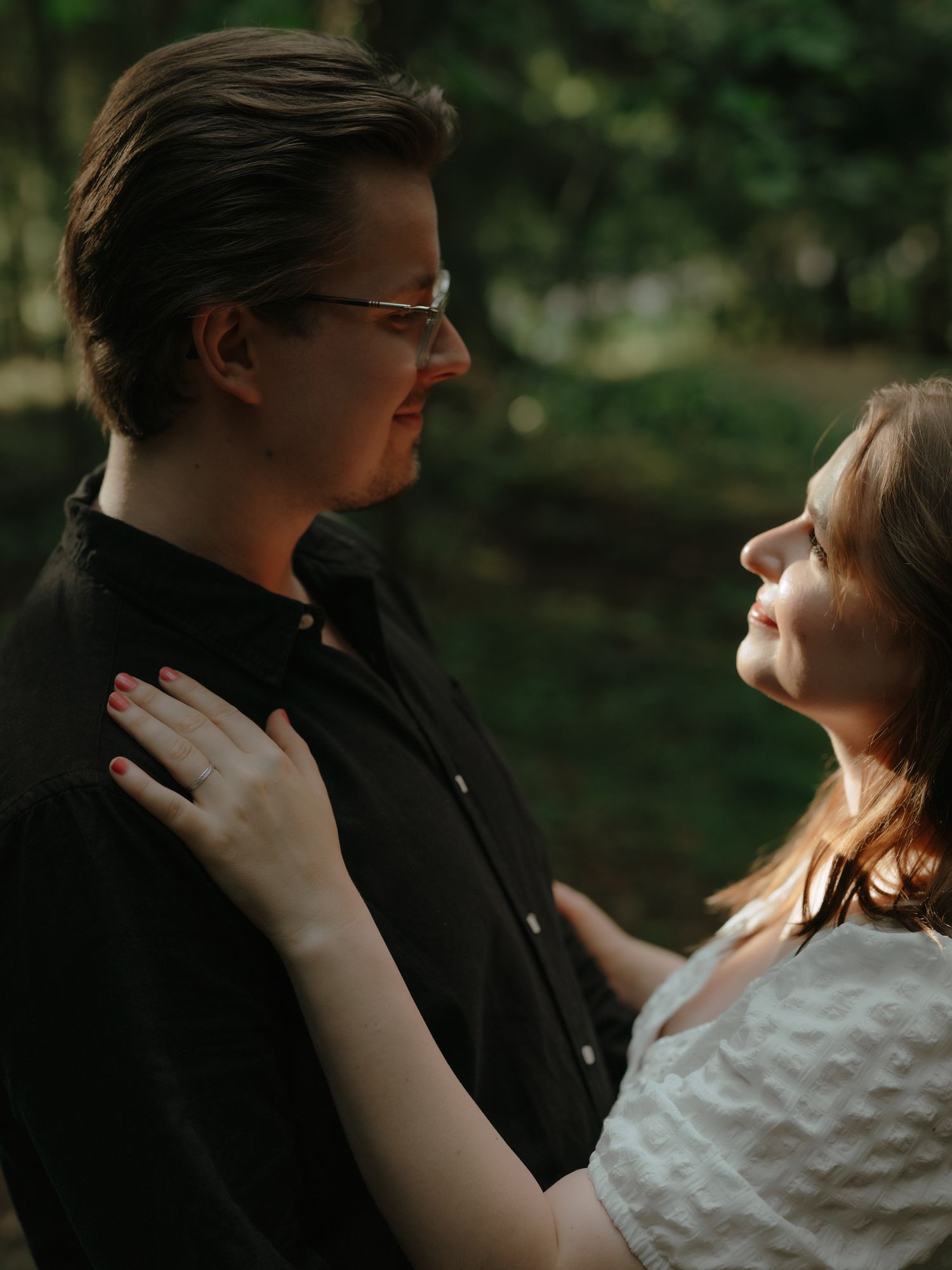 Intimate couple embraces in romantic outdoor portrait with soft lighting and natural bokeh background.