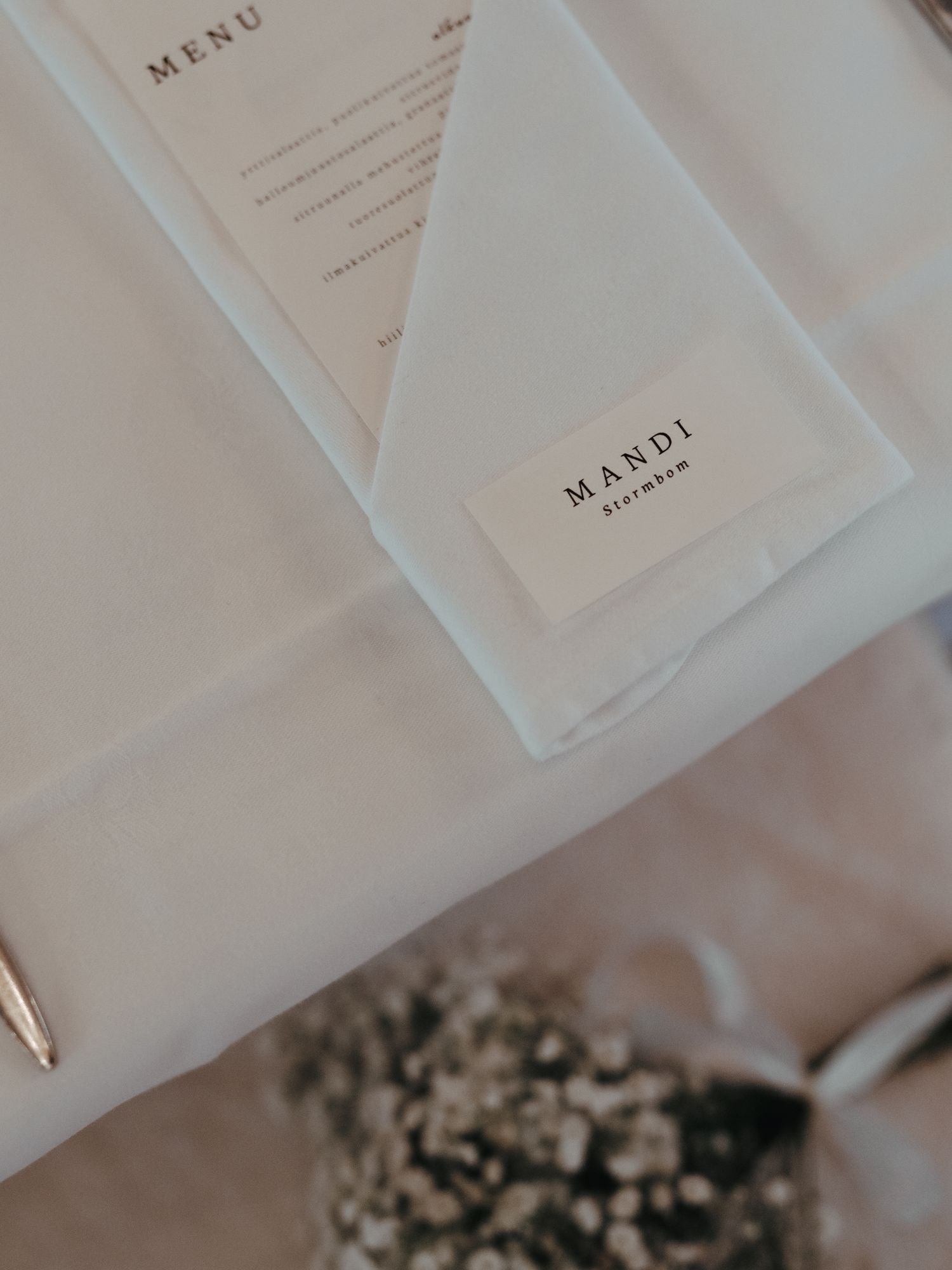 A minimalist wedding menu and place card on a white tablecloth with dried flowers in soft focus.