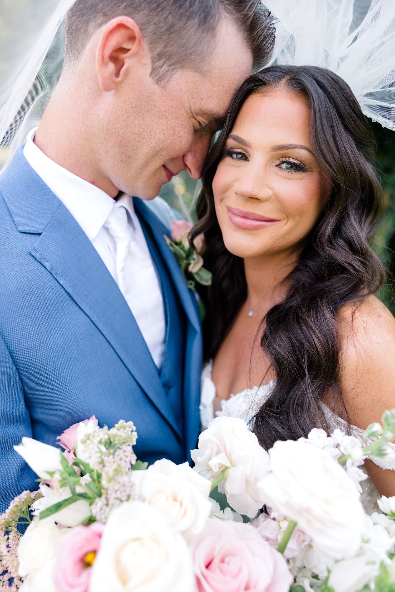An intimate wedding portrait showing a tender moment between newlyweds with floral bouquet.