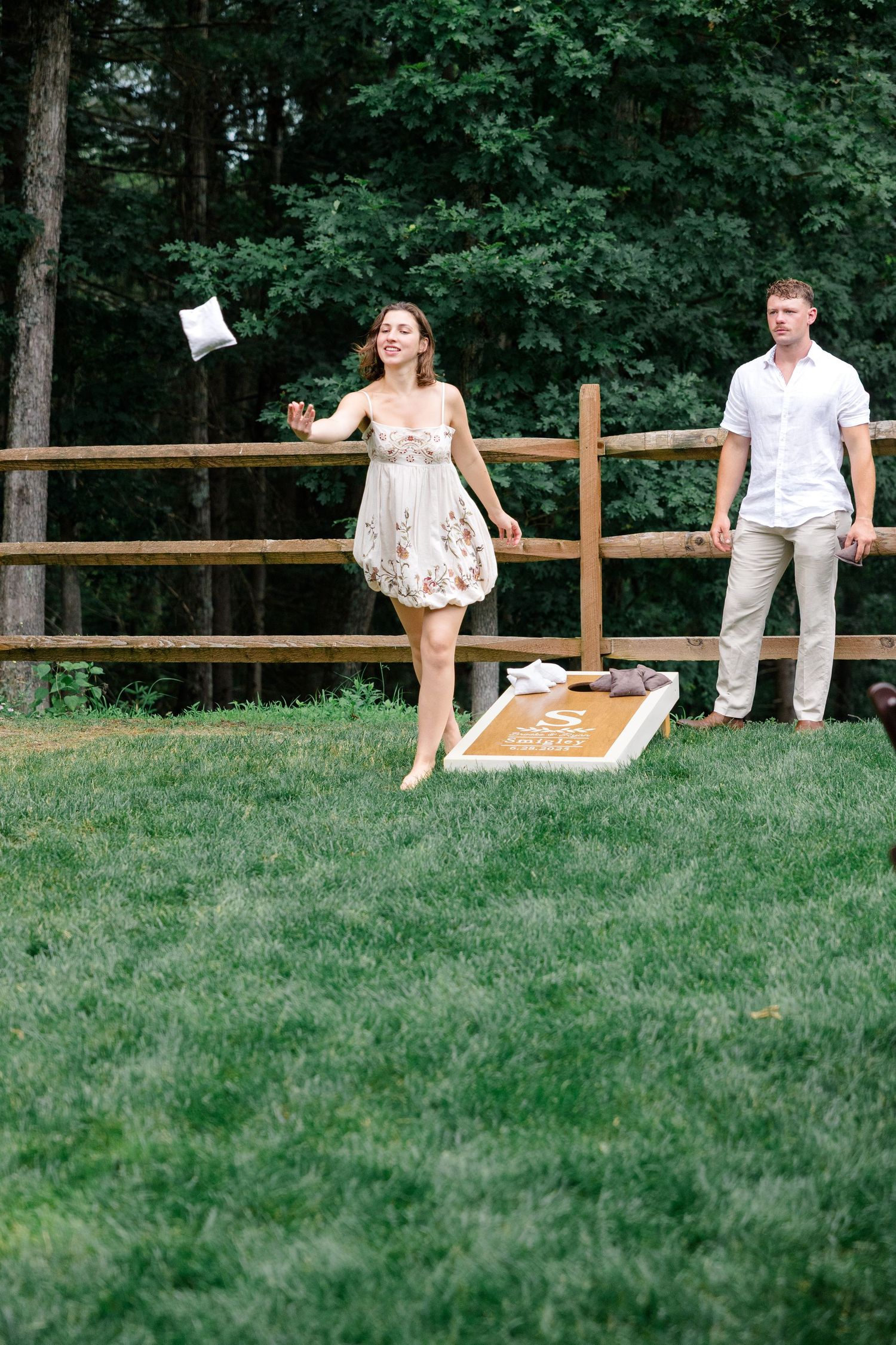 Wedding party sitting casually on wooden fence in outdoor garden setting.