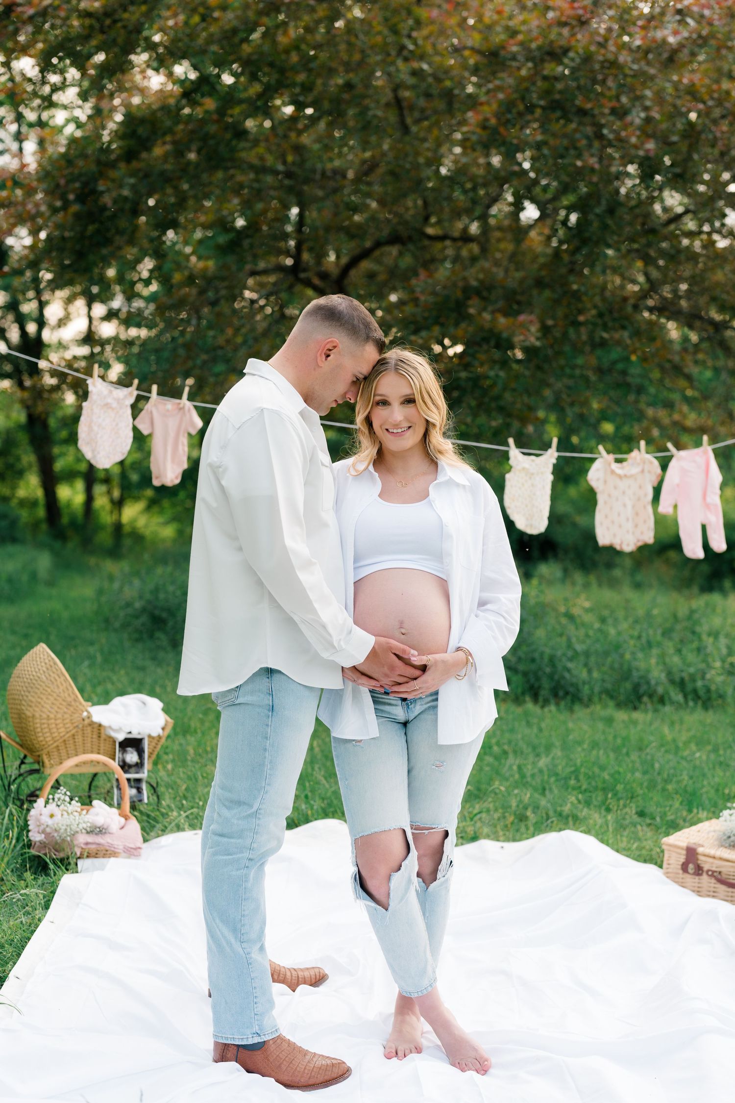 Maternity photoshoot in garden with baby clothes hanging on clothesline in background.