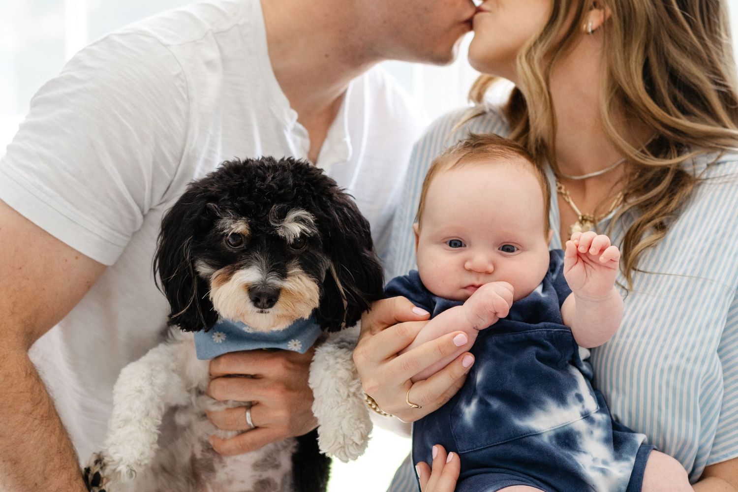 Small black and white dog poses with family in white casual clothing and tie-dye while snuggling together.
