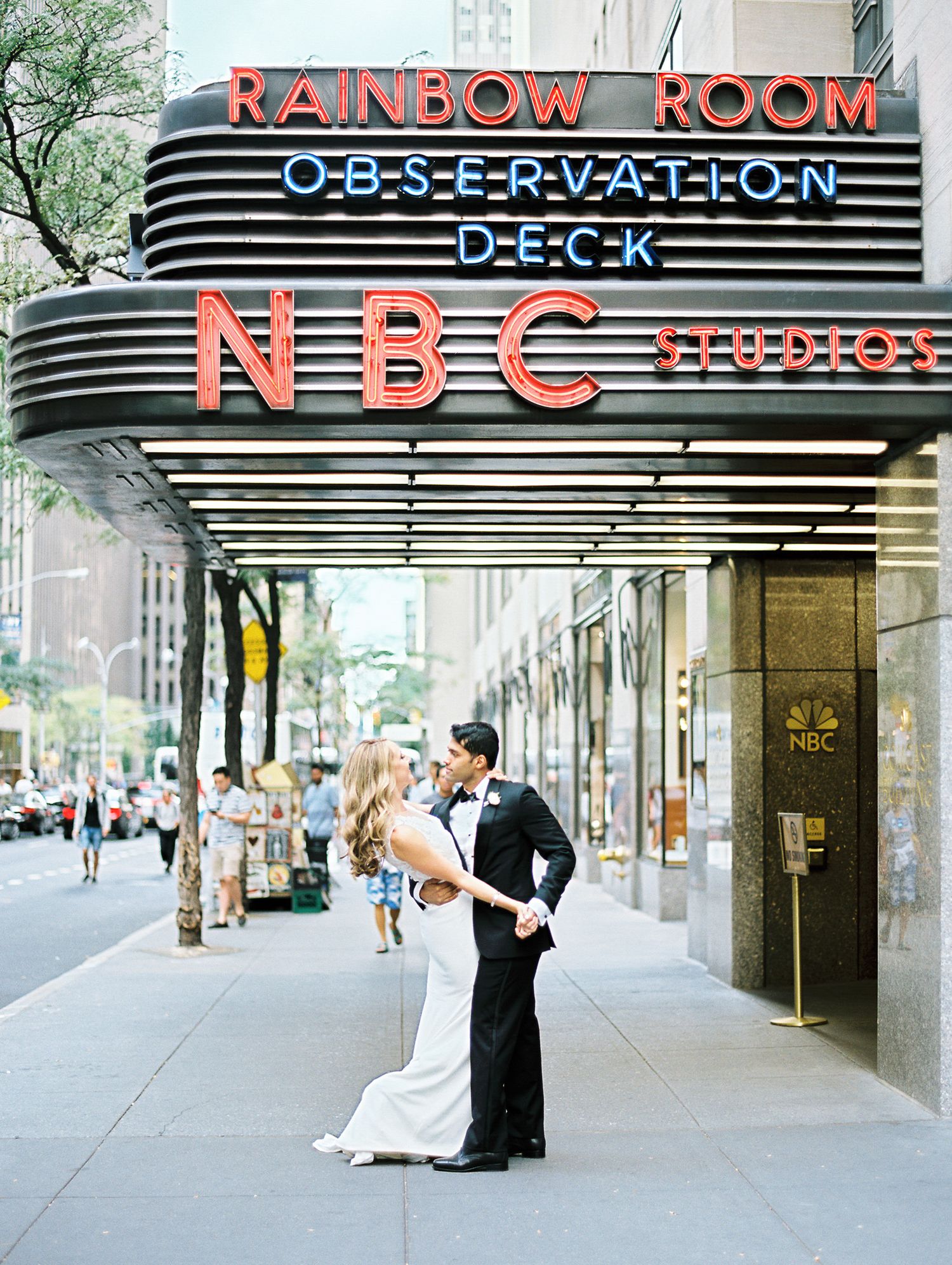 Wedding couple embracing under the iconic NBC Rainbow Room sign in New York City.